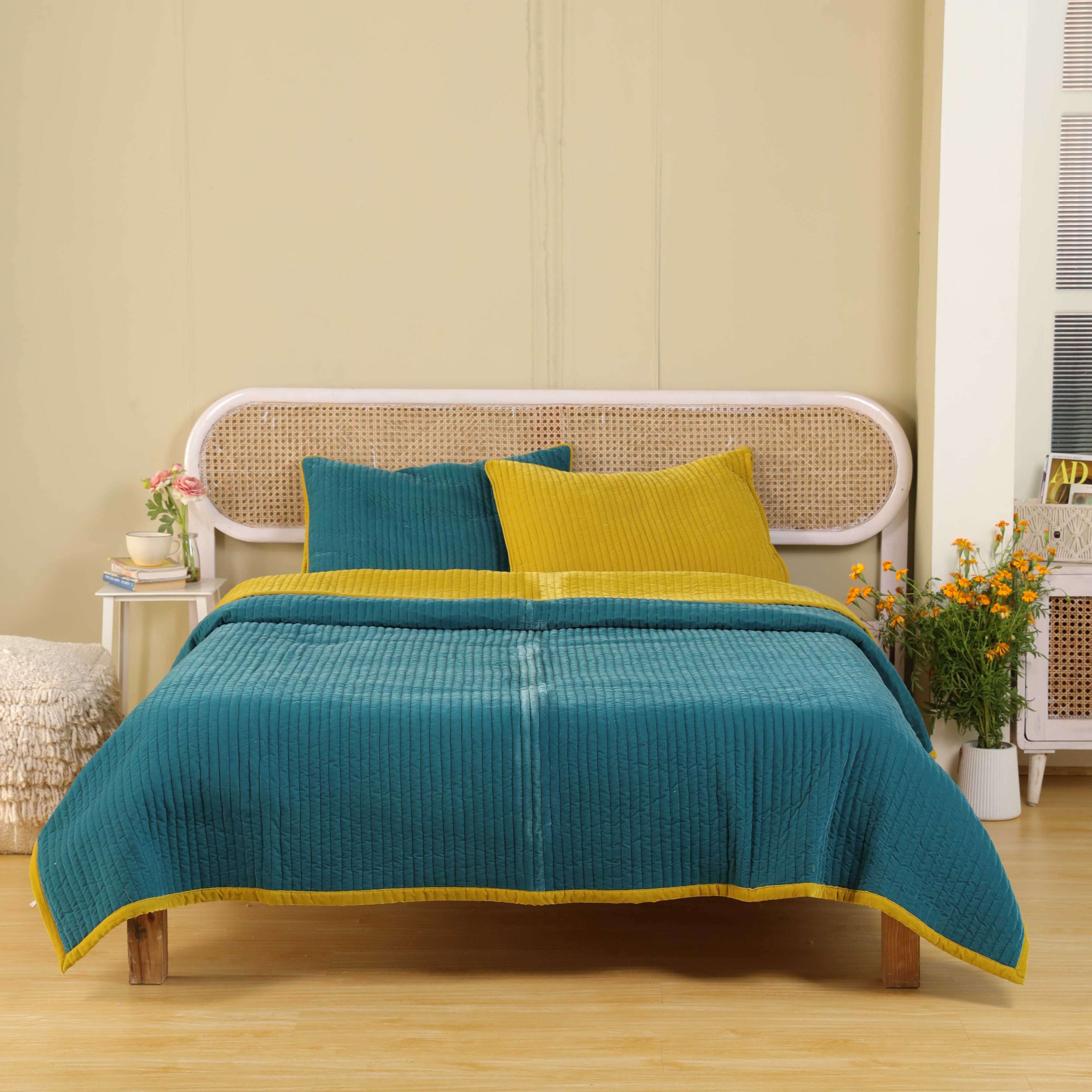 Matching teal blue and mustard yellow quilted velvet pillow covers resting on a white sheet.