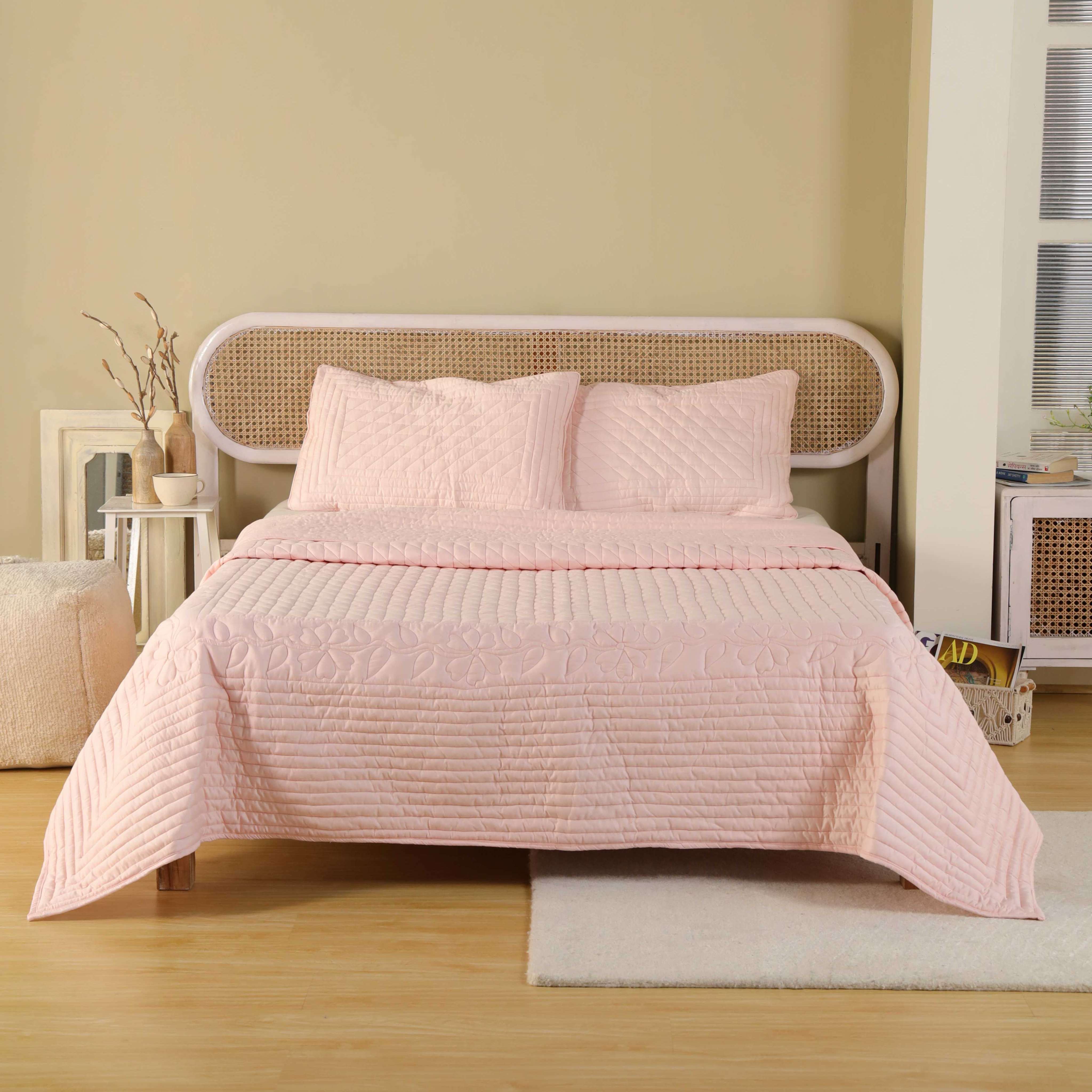 A luxurious blush pink satin quilt set with floral quilting on a bed with a rattan headboard.