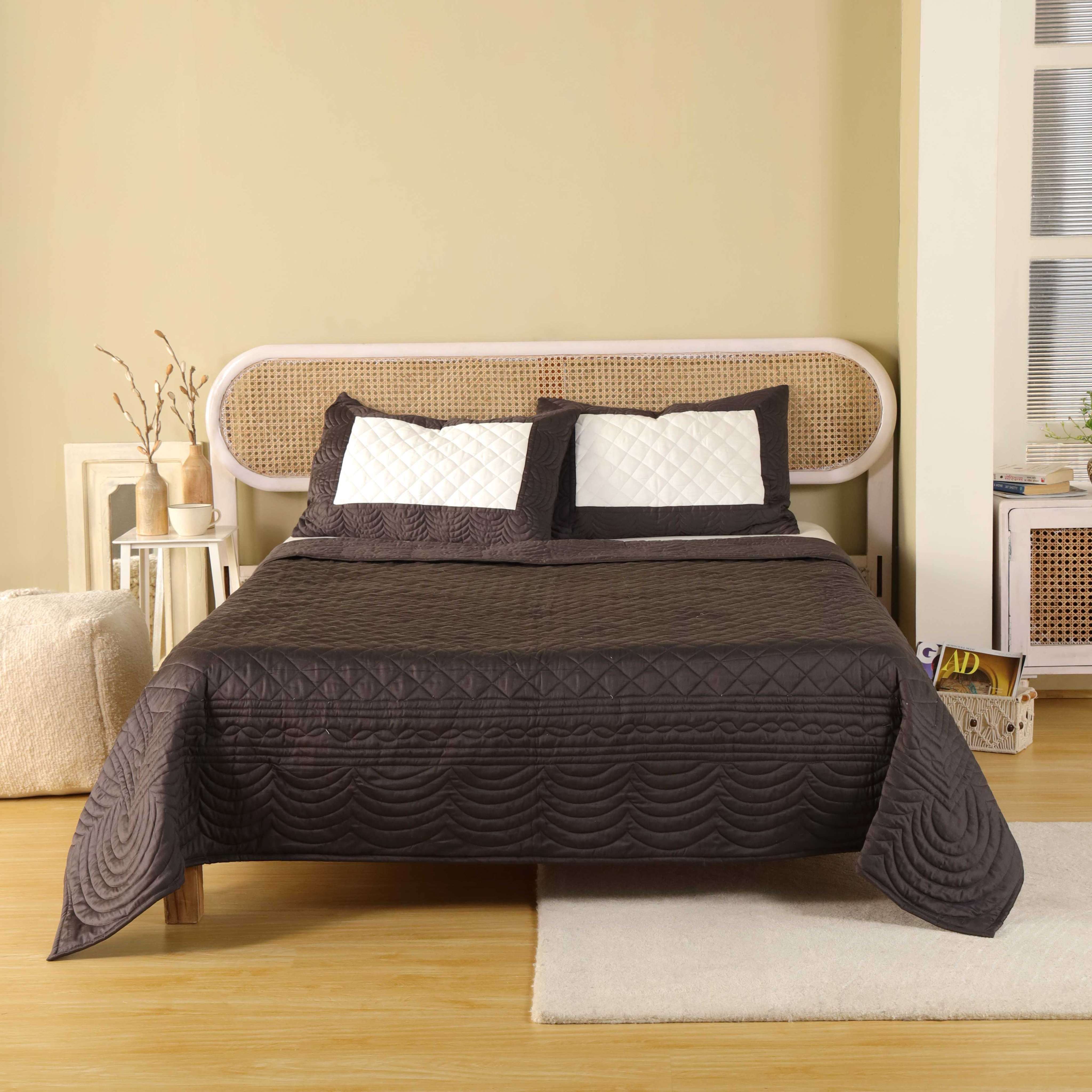 A rich chocolate brown satin quilt set with scalloped patterns on a bed with a rattan headboard.