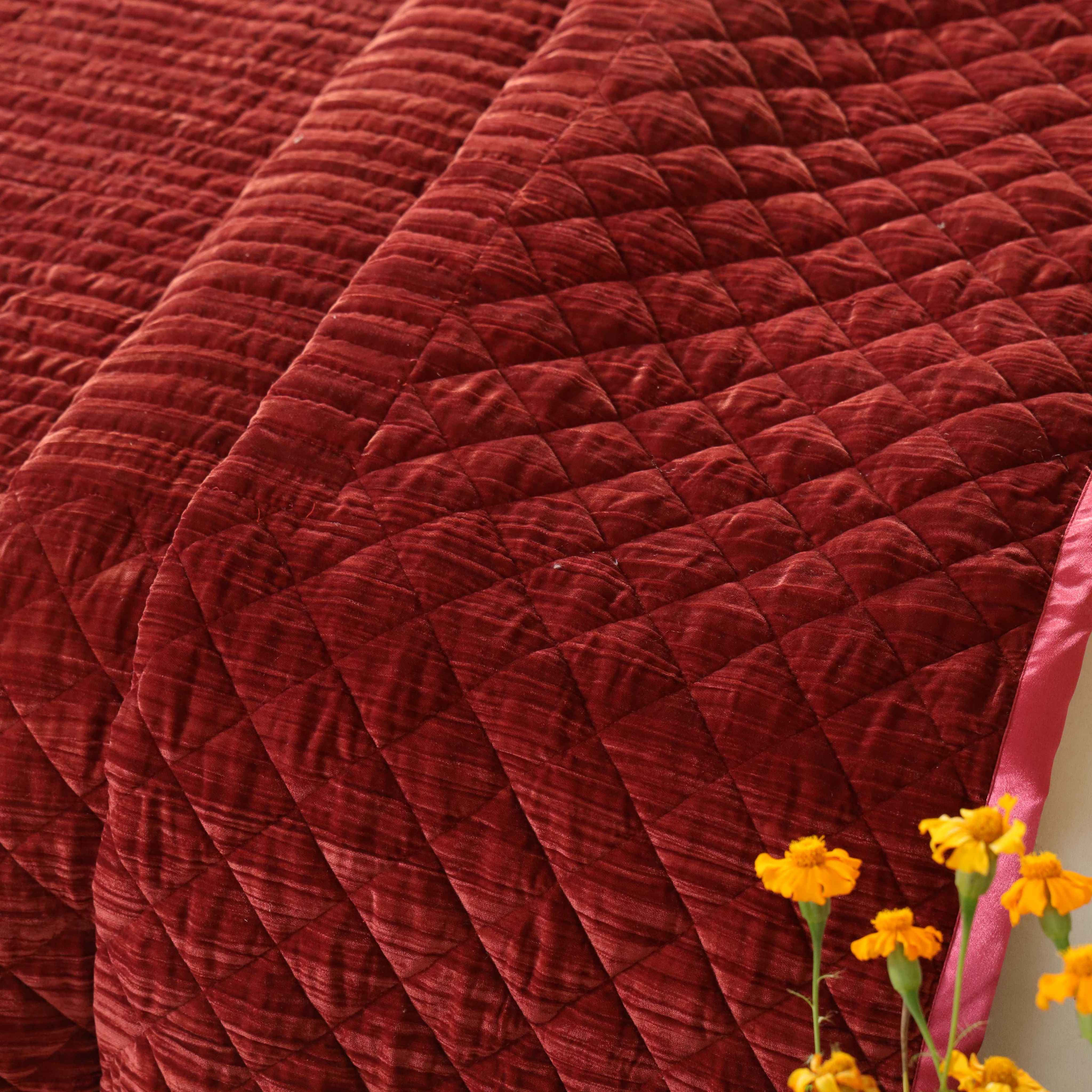 Close-up of plush velvet fabric showing the faded maroon color and detailed diamond stitching.