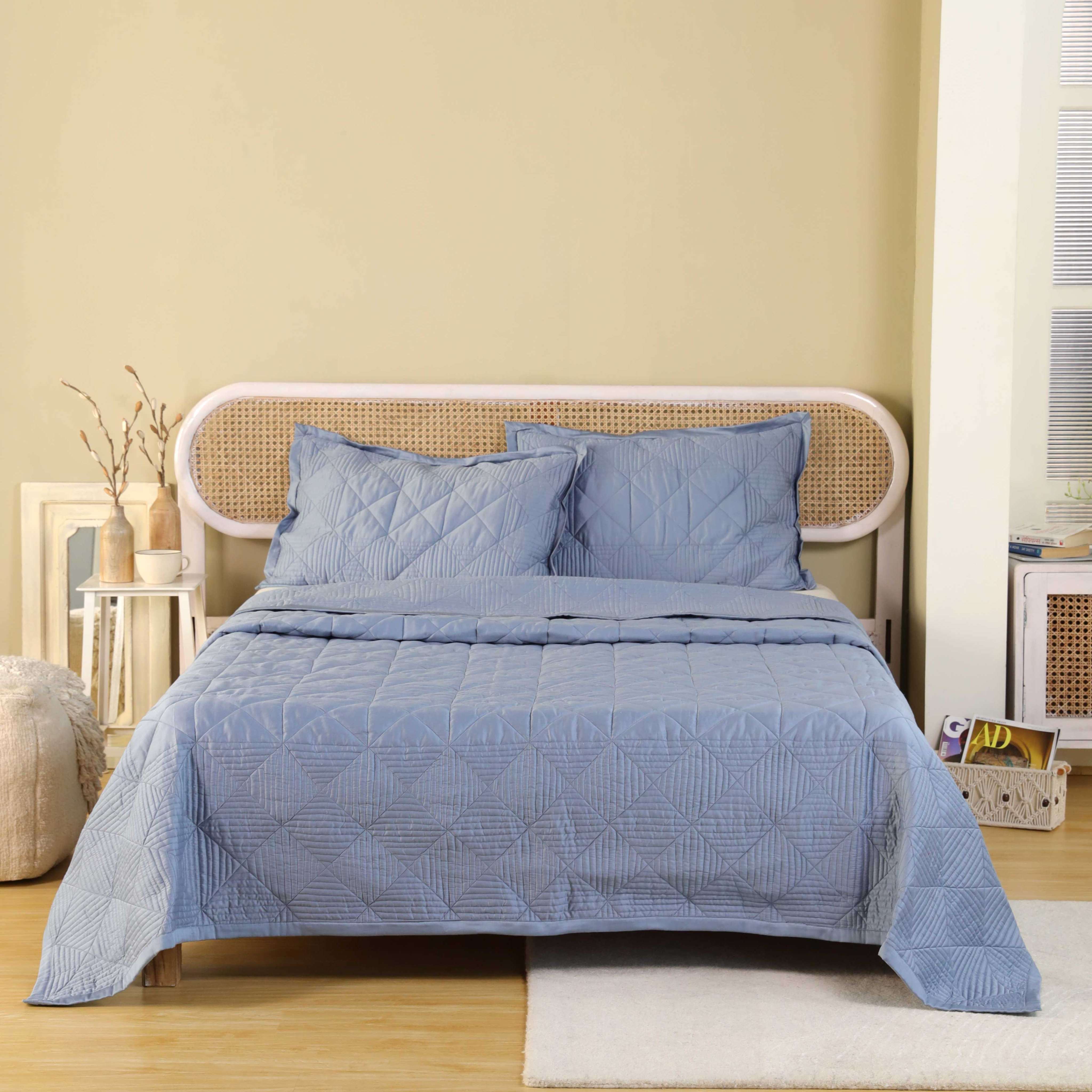 A dusty blue velvet quilt set with a modern geometric square pattern on a bed.