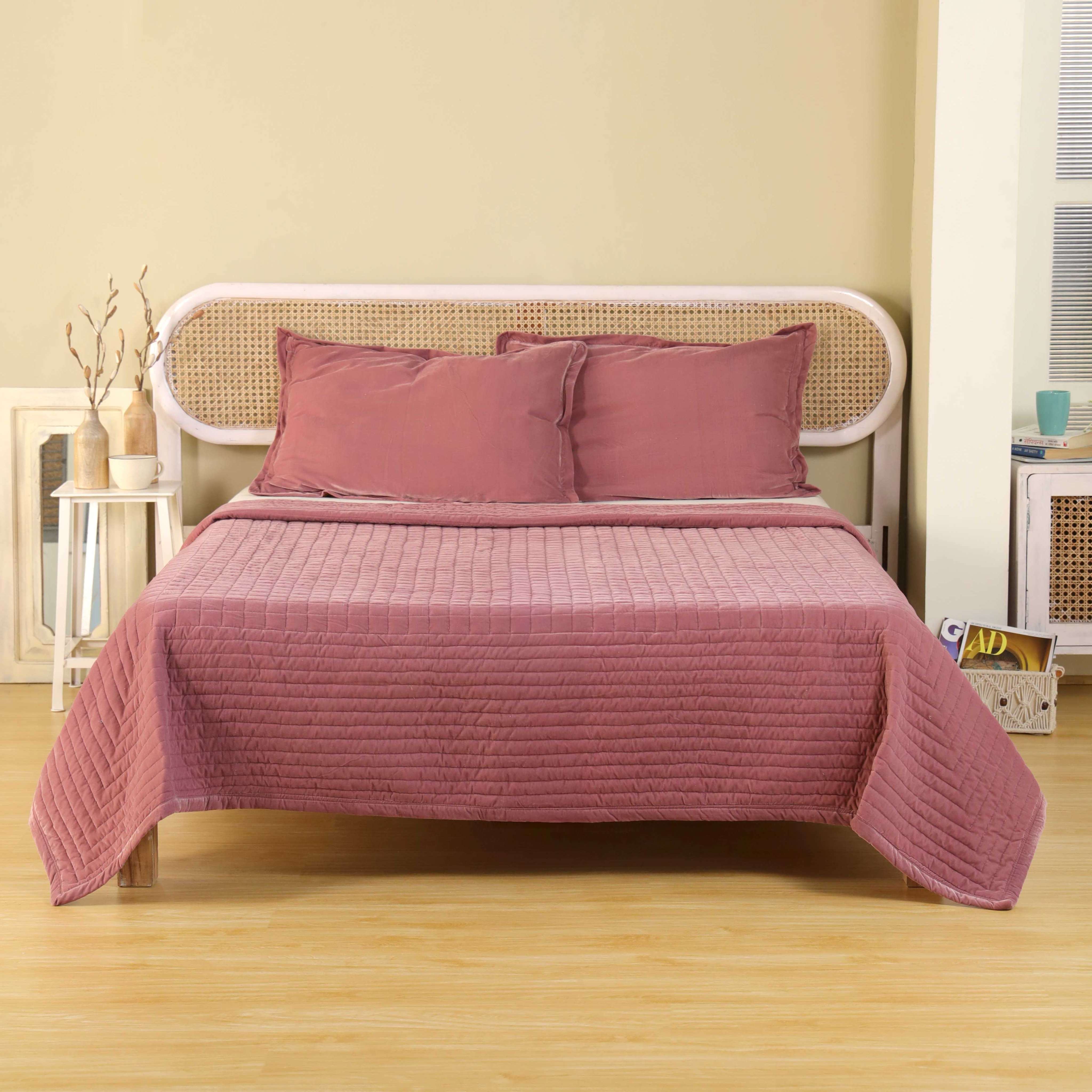 Dusty pink velvet duvet cover with horizontal quilting on a bed with a white cane headboard.