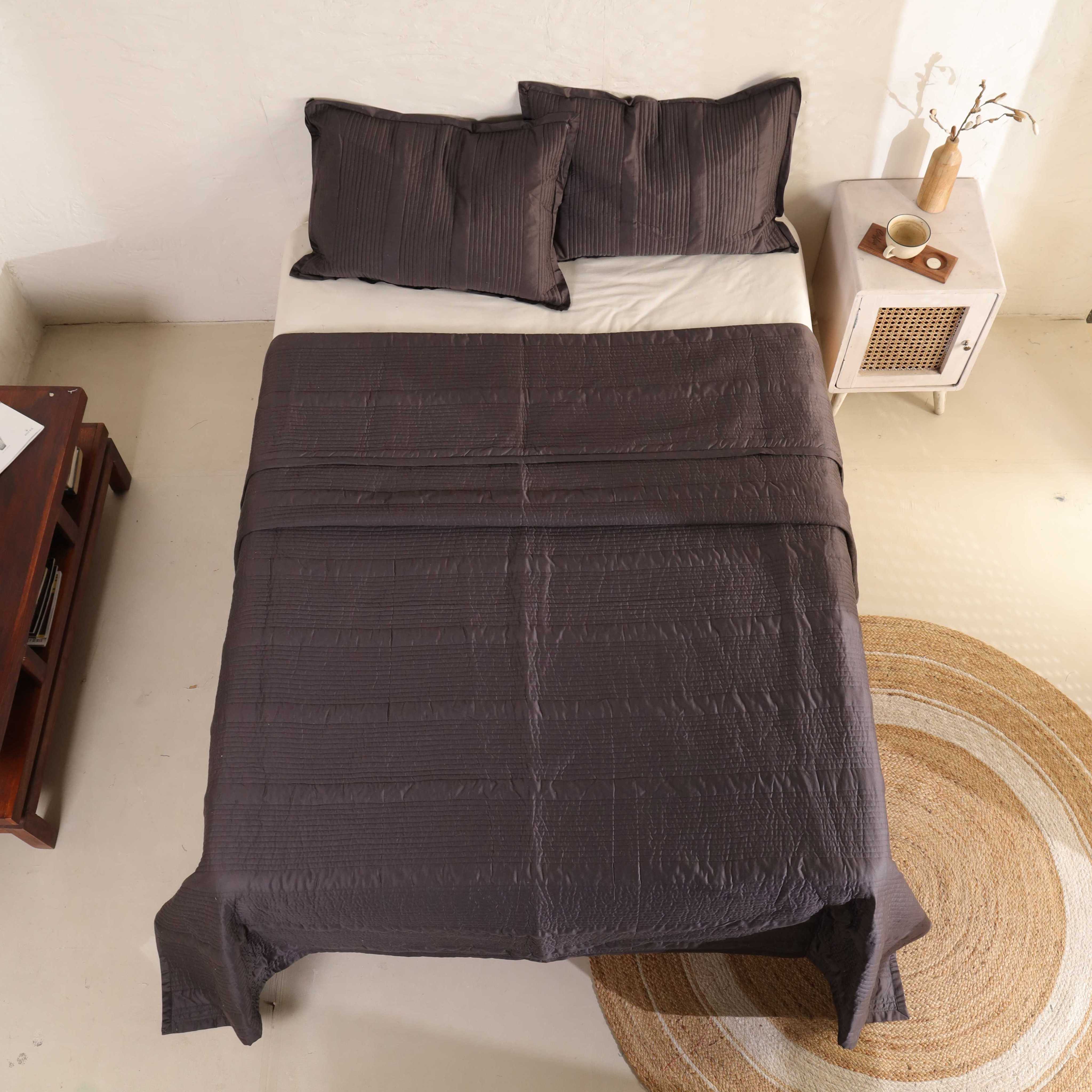 Two matching coffee brown velvet pillow covers resting on a textured quilt.