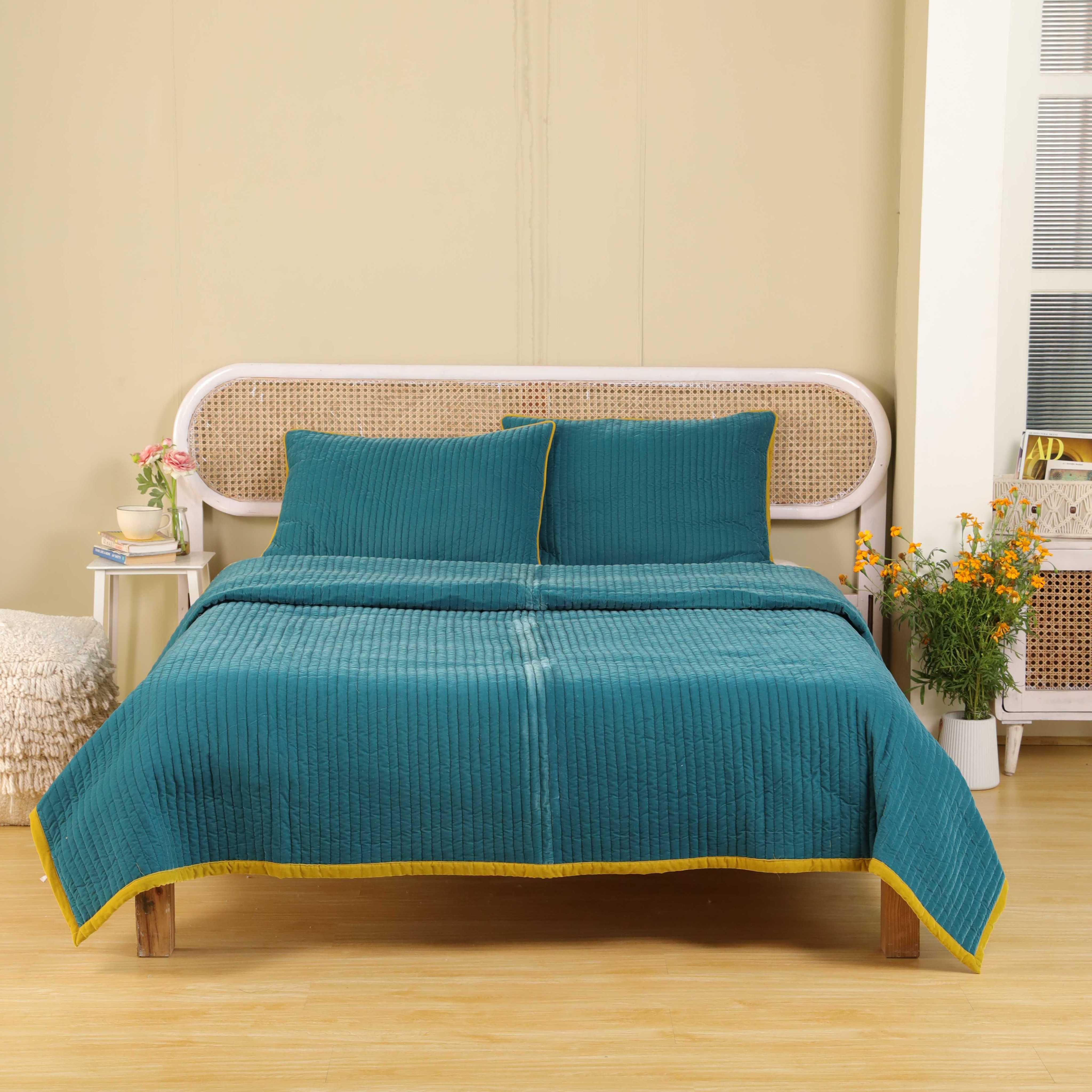 Luxury teal blue quilted bedding set styled in a bright modern bedroom with warm wood accents.