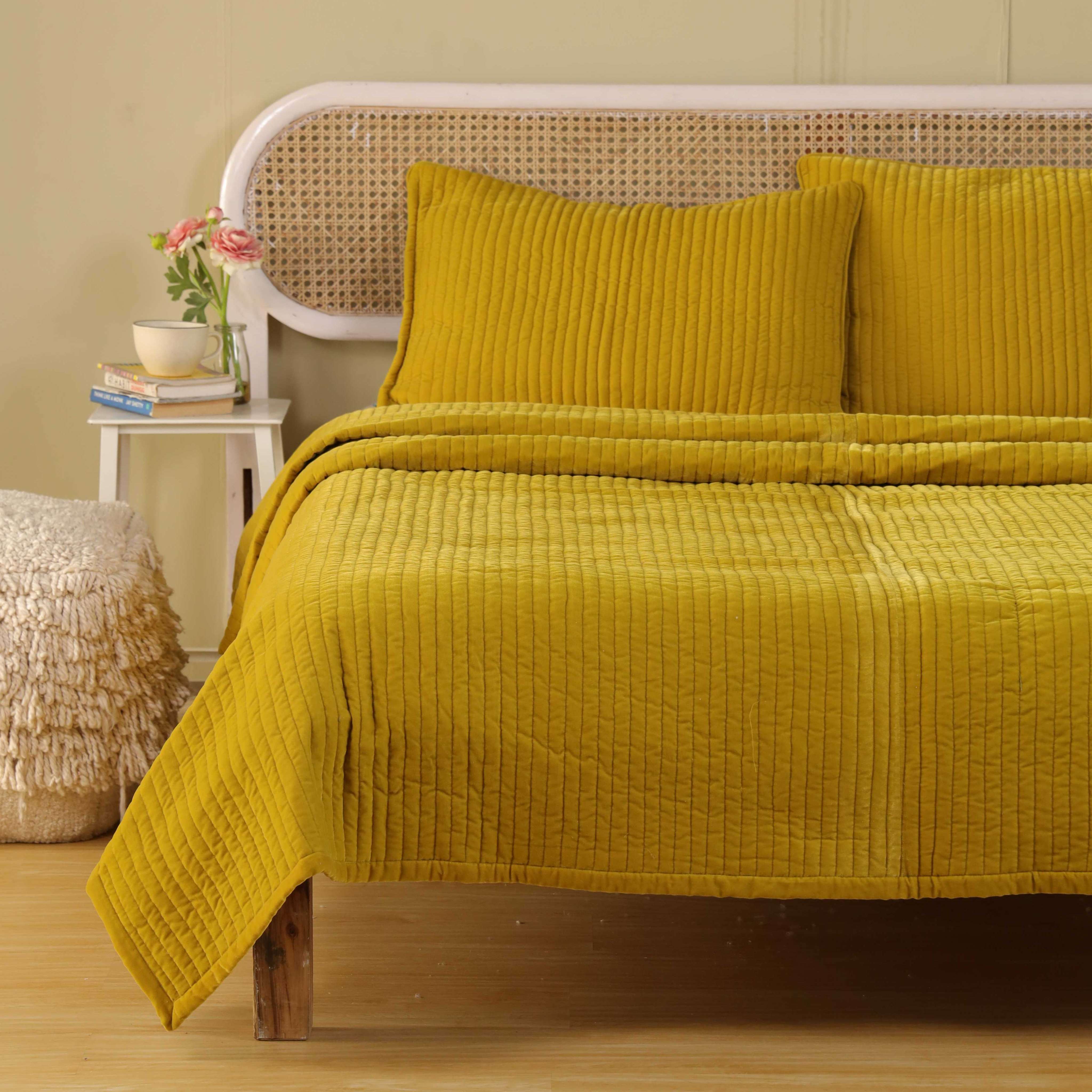 A bright modern bedroom featuring luxury mustard yellow quilted bedding and minimalist decor.