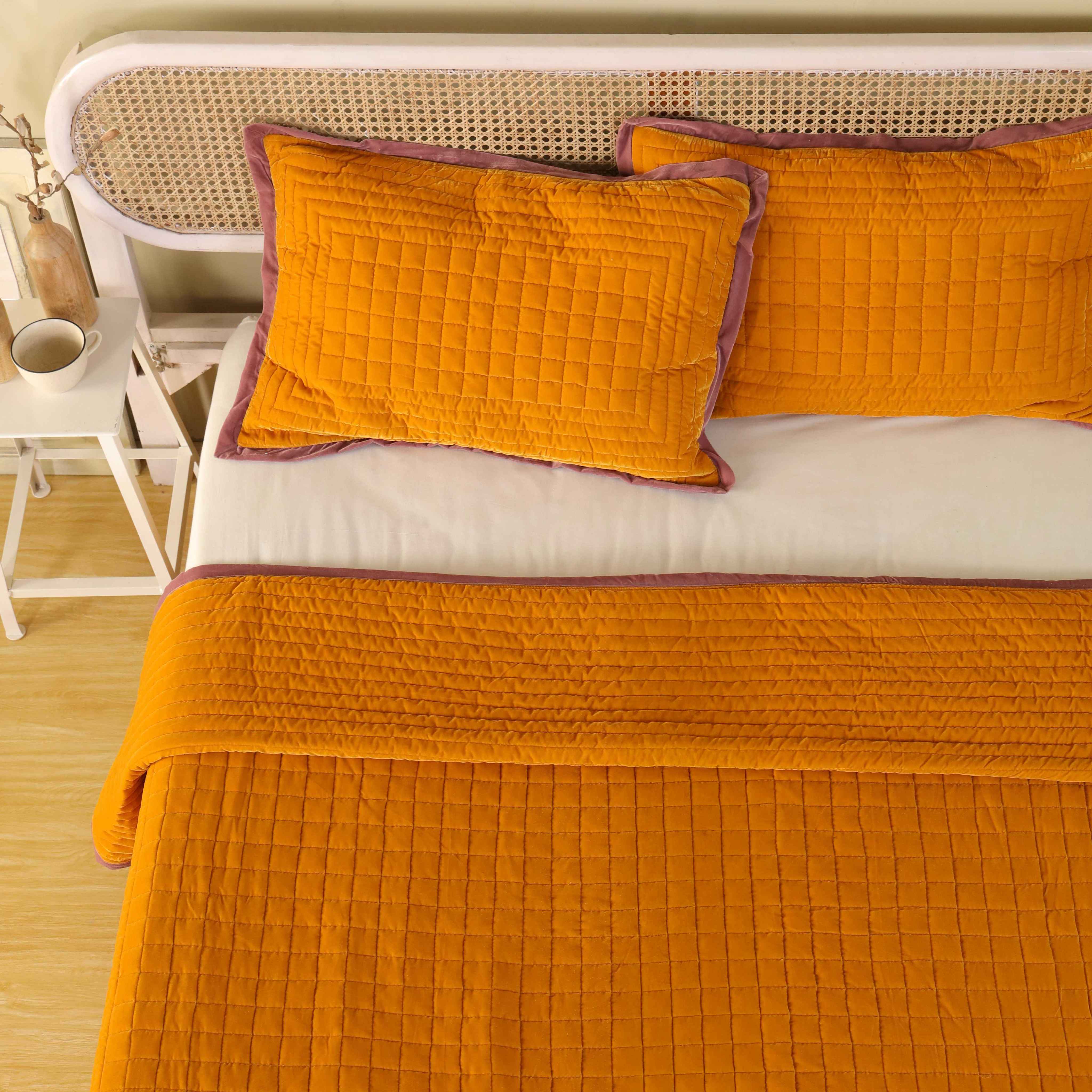 Luxury mustard yellow quilted bedding set styled in a bright minimalist bedroom with a cane headboard.