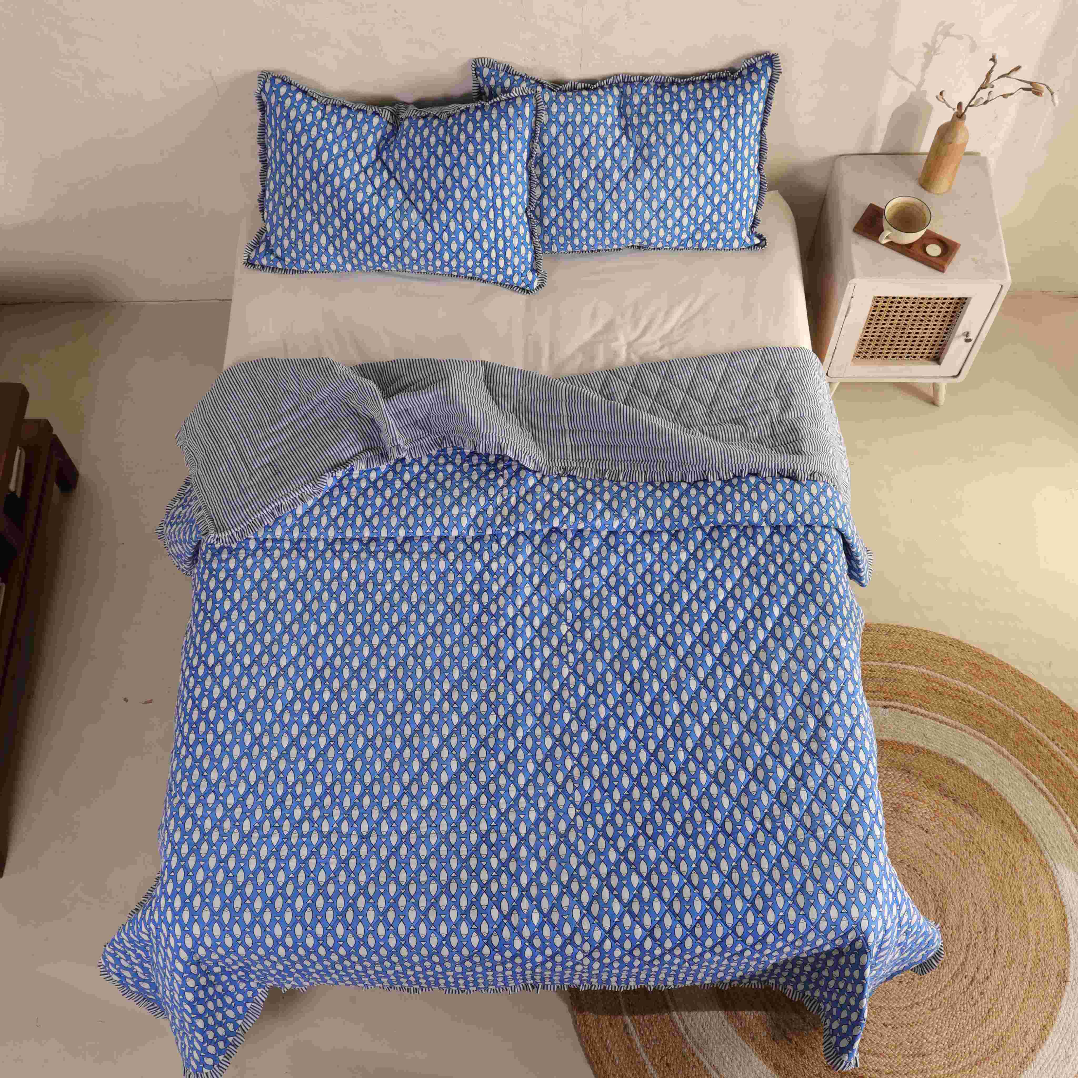 Coastal bedroom interior featuring a blue velvet quilt and natural jute rug.