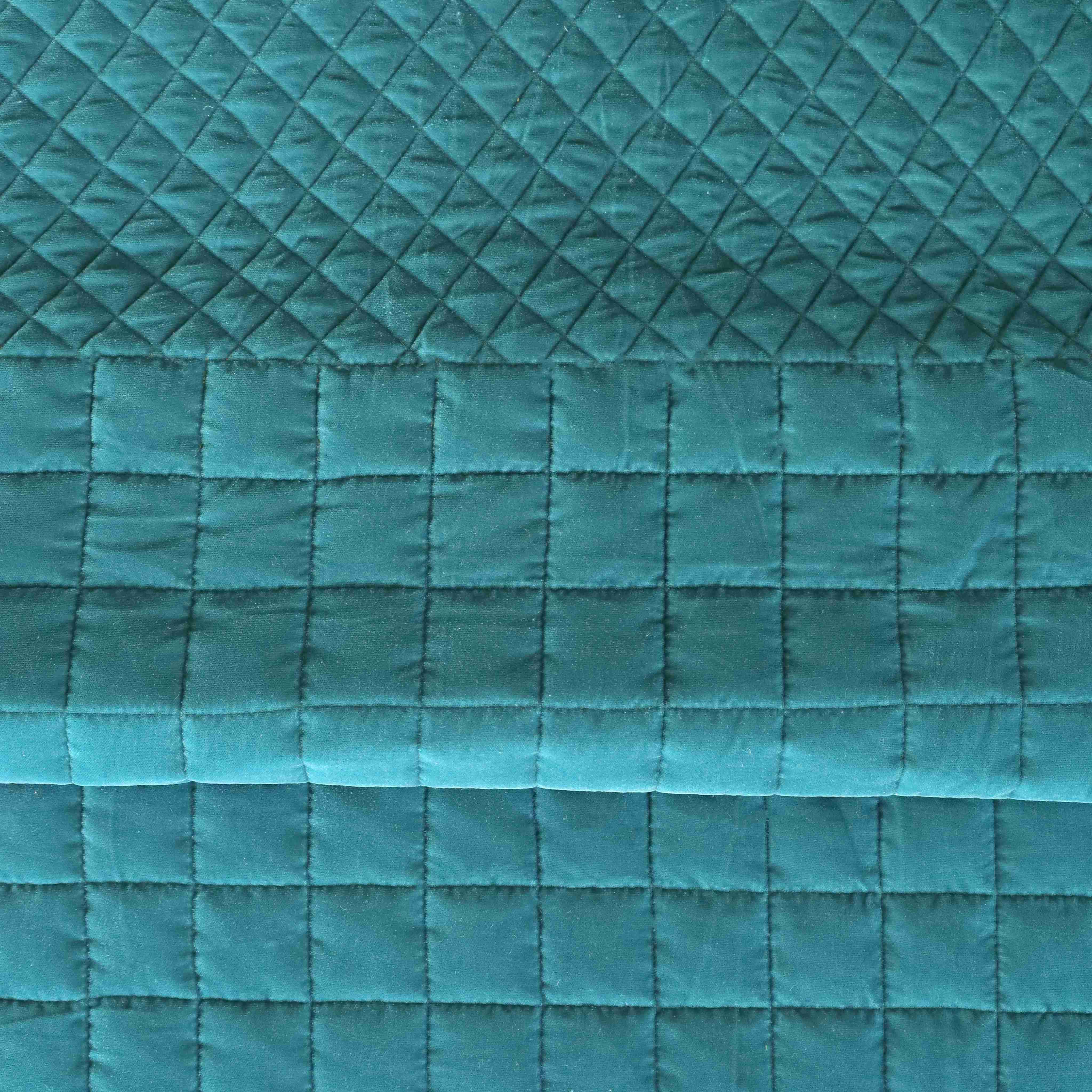 Teal blue velvet quilt set styled with a cane headboard in a minimalist bedroom.