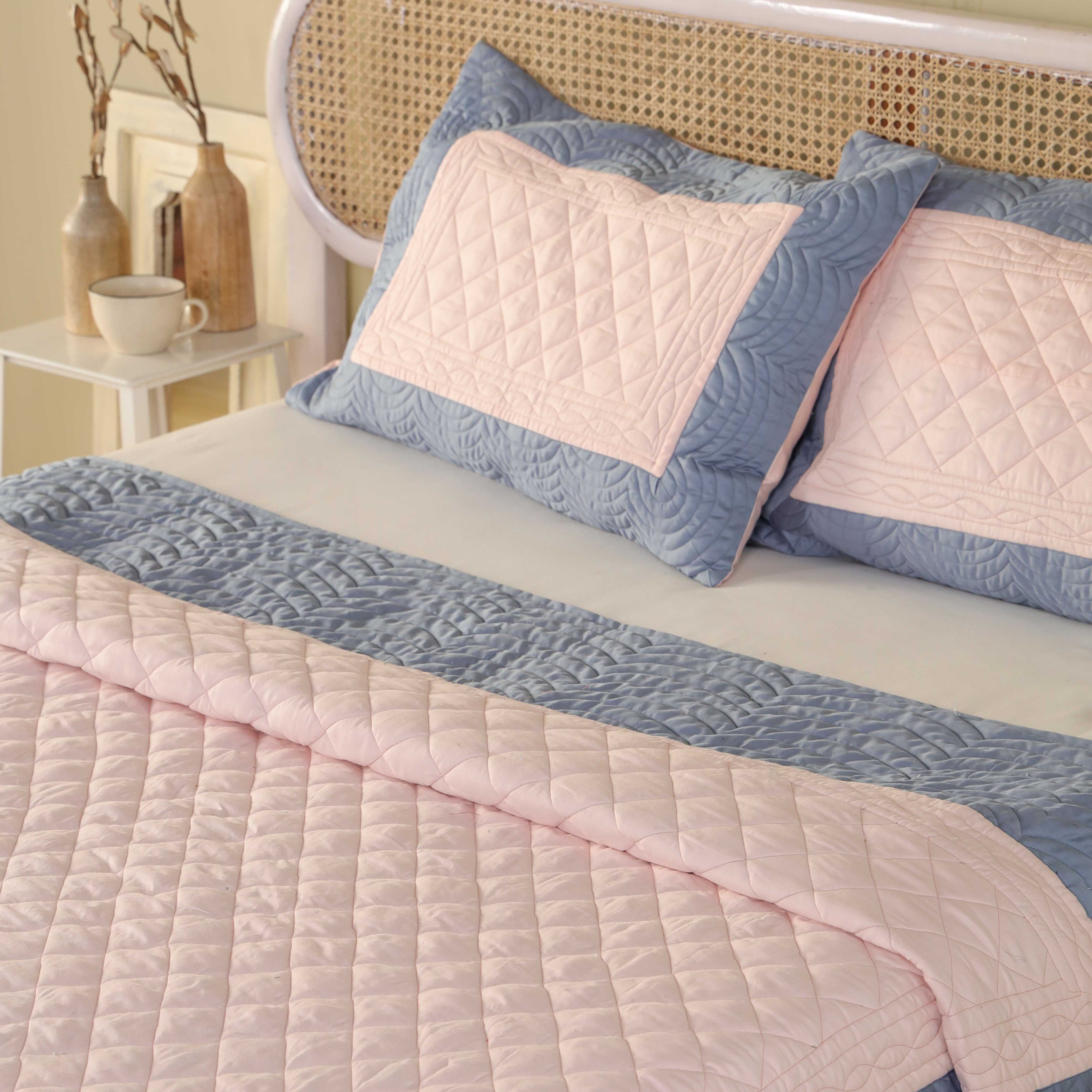 A styled bedroom featuring a blue and pink satin quilt set with minimalist neutral decor.