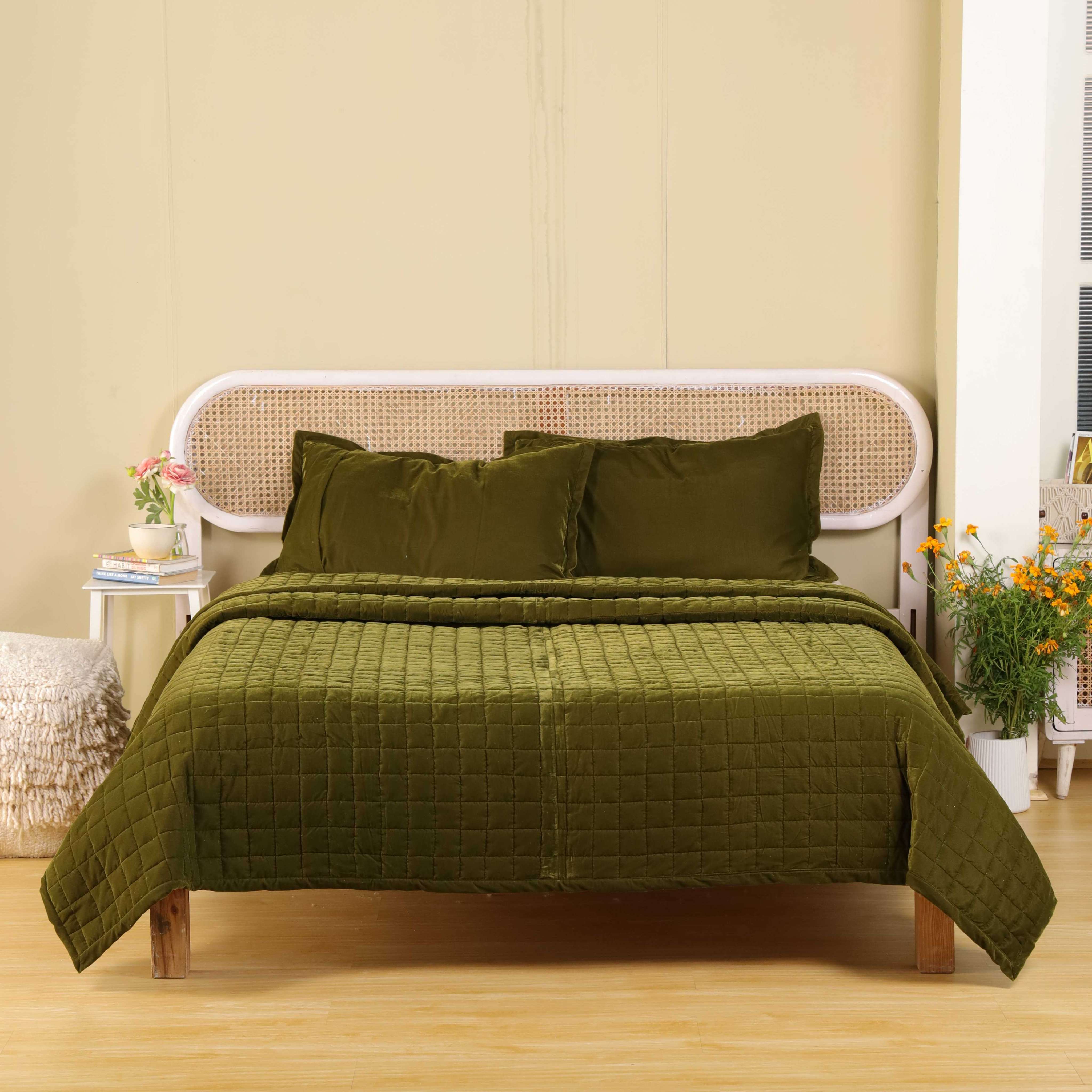 Dark olive green velvet quilt set on a wooden bed frame with a rattan headboard.