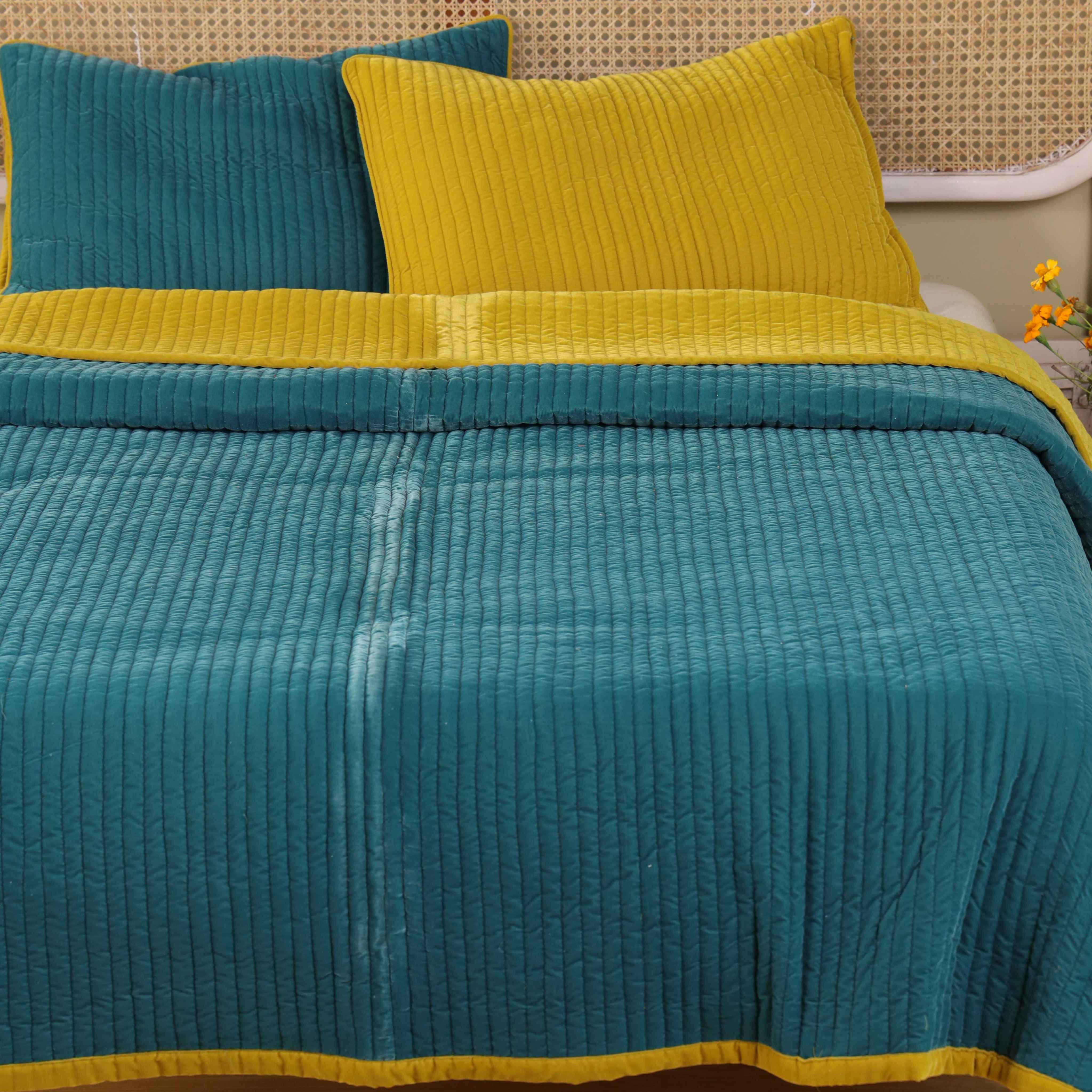 Luxury reversible bedding set in teal and yellow styled on a bed with a modern cane headboard.