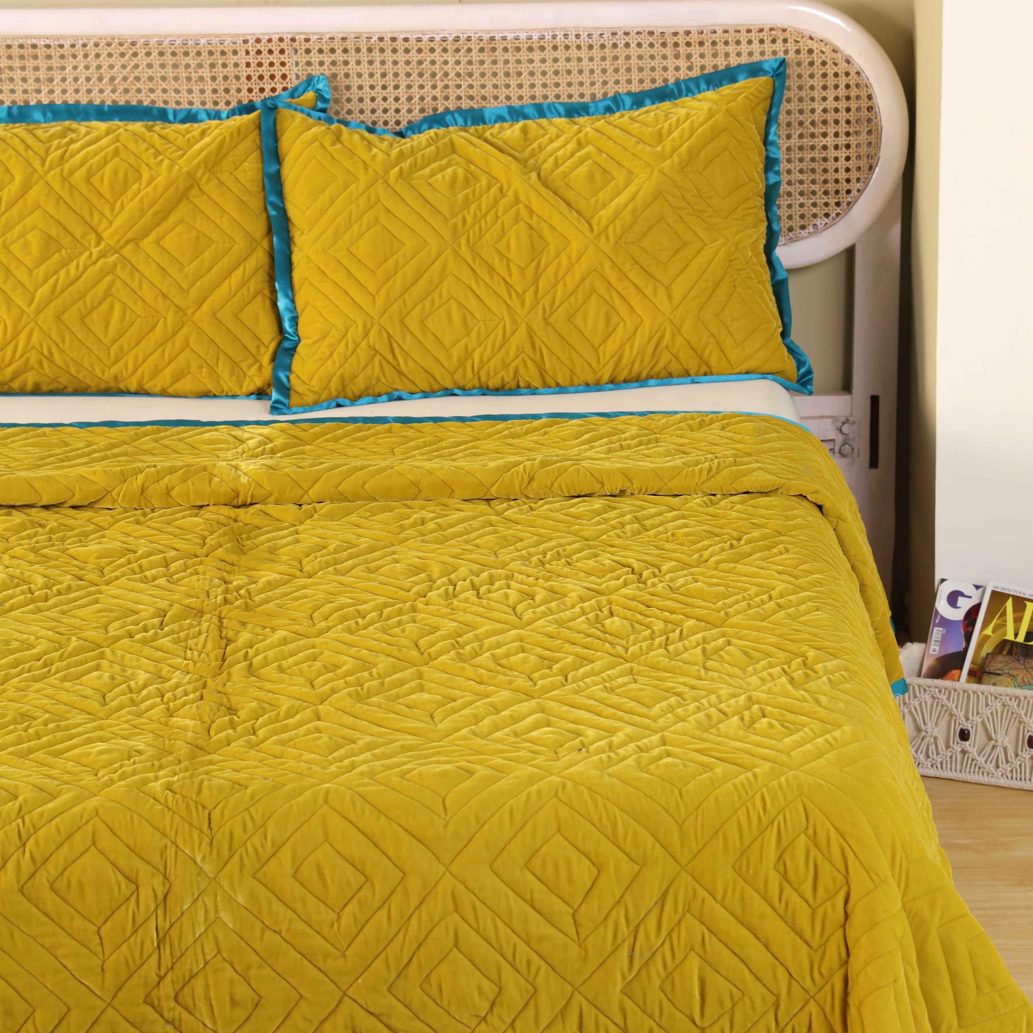 Matching mustard yellow satin pillow covers featuring geometric quilting and teal blue trim.