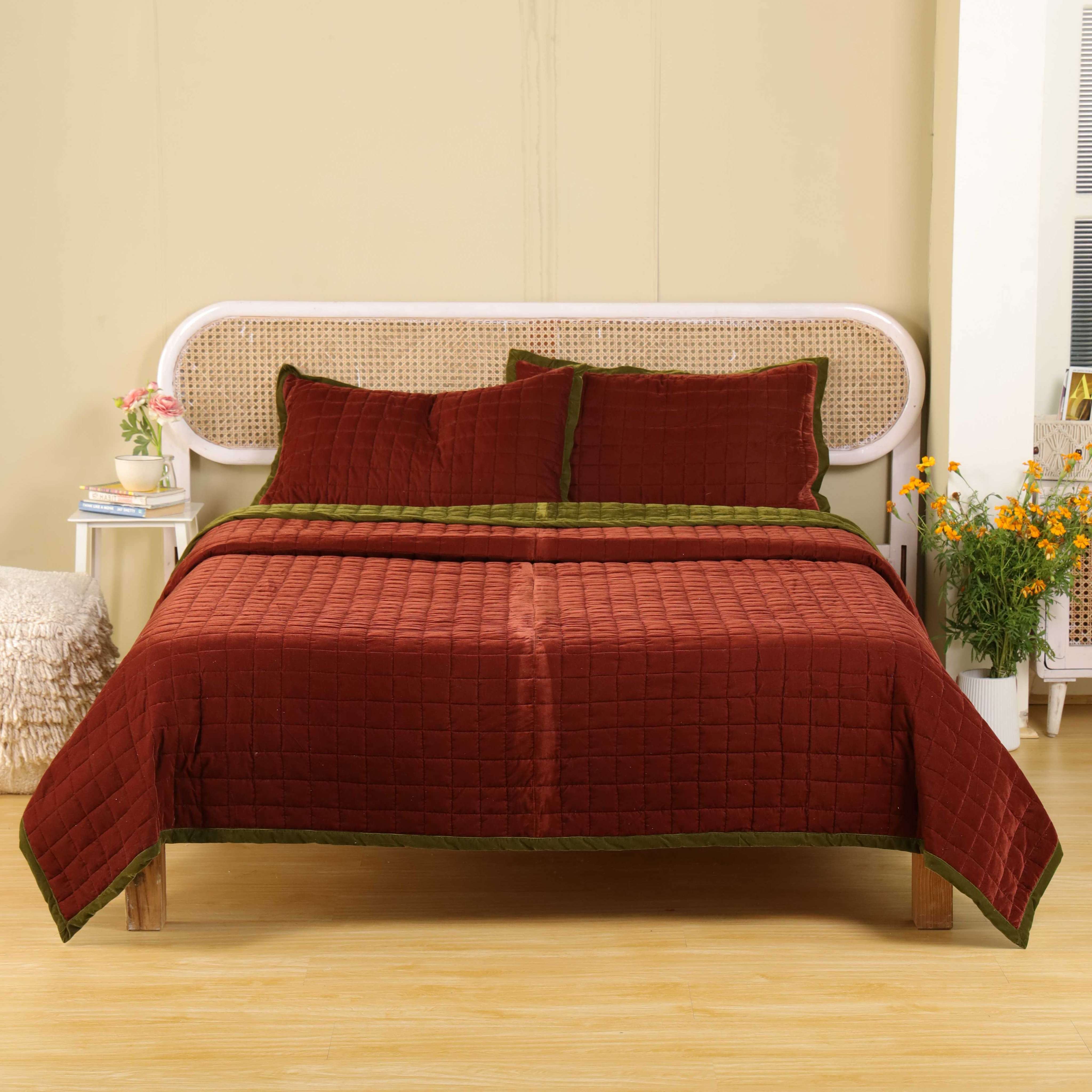 Reversible brick red and olive green velvet quilt set on a bed with a rattan headboard.