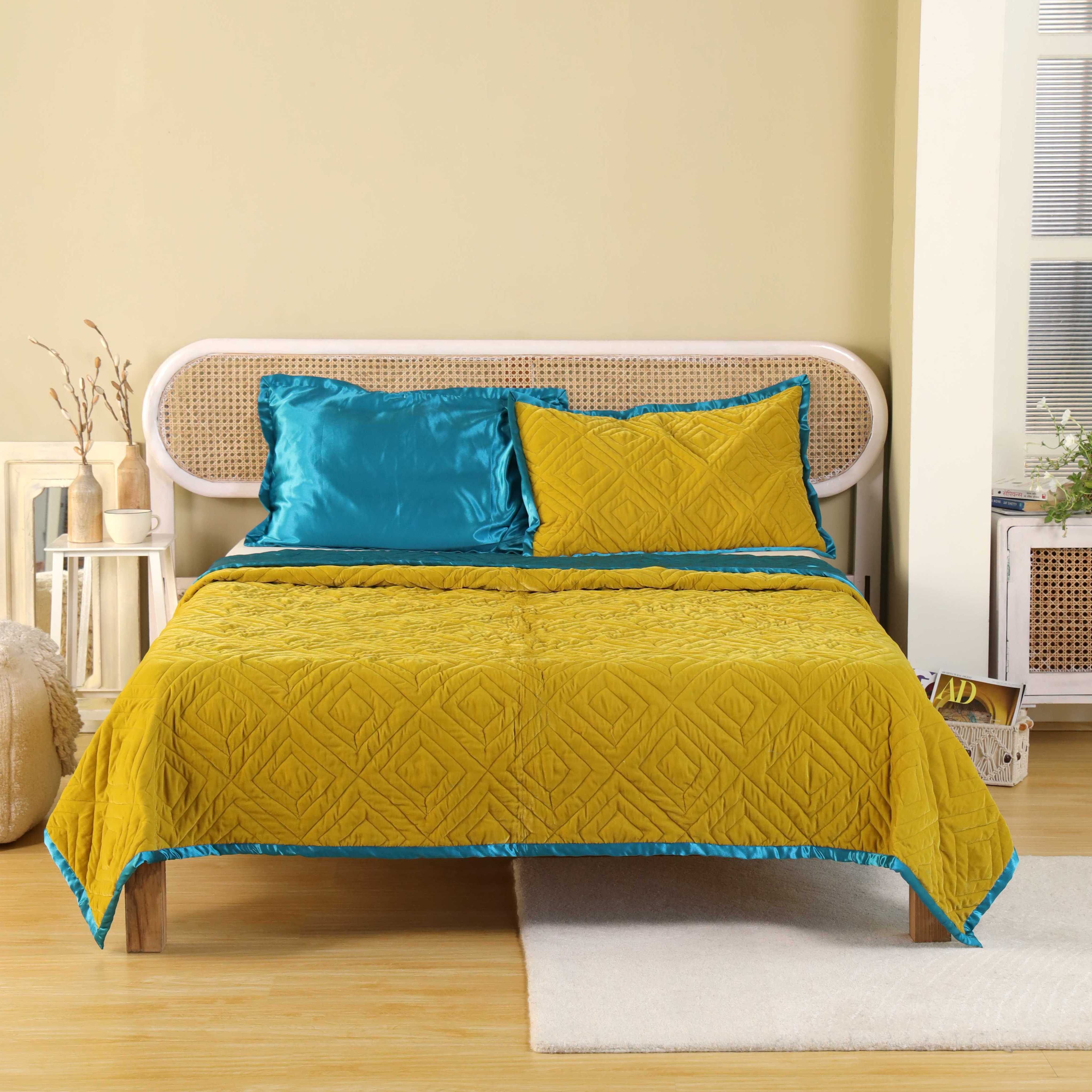A reversible mustard yellow velvet quilt with teal blue satin trim on a bed.