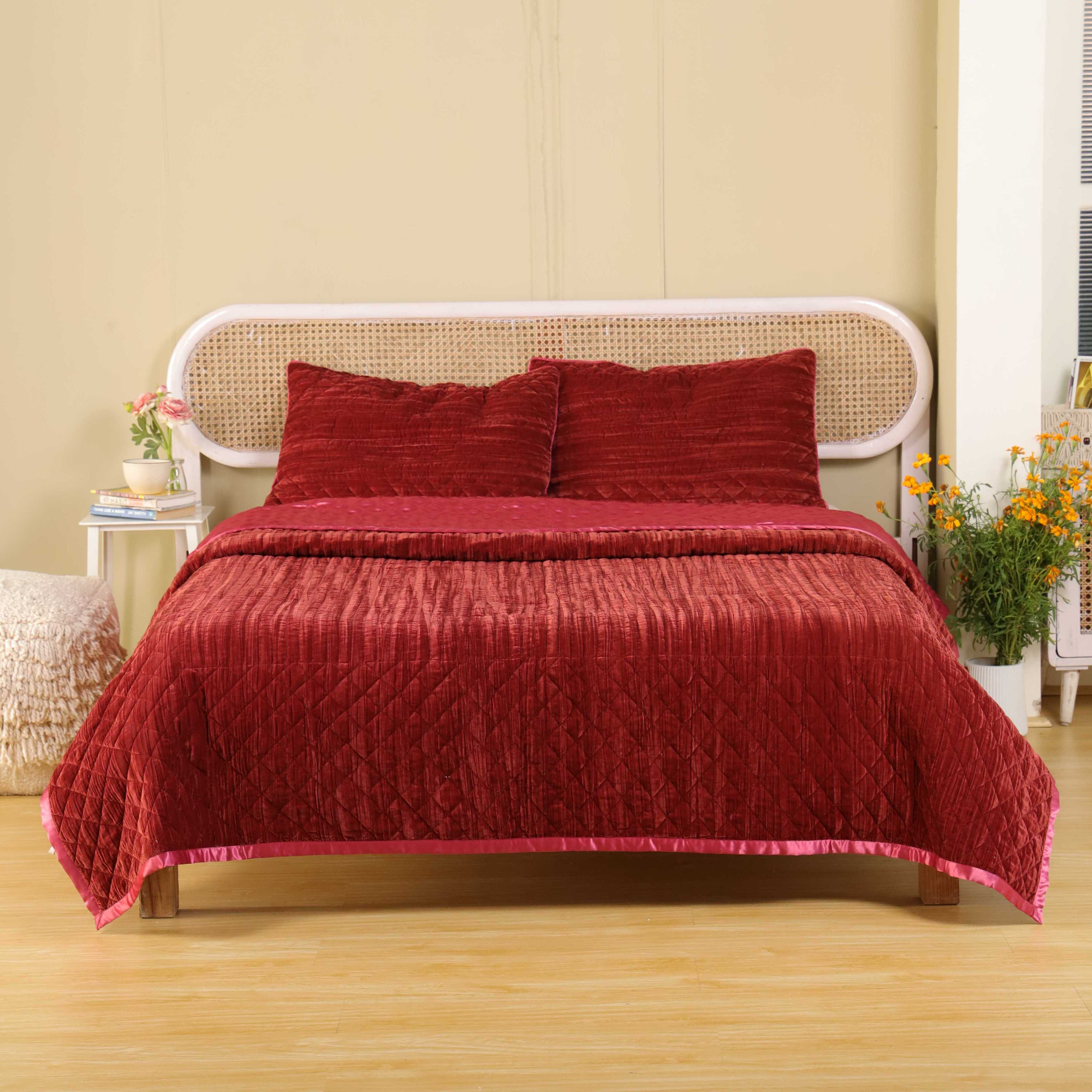 Reversible faded maroon quilt set with one side velvet and one side satin on a bed.