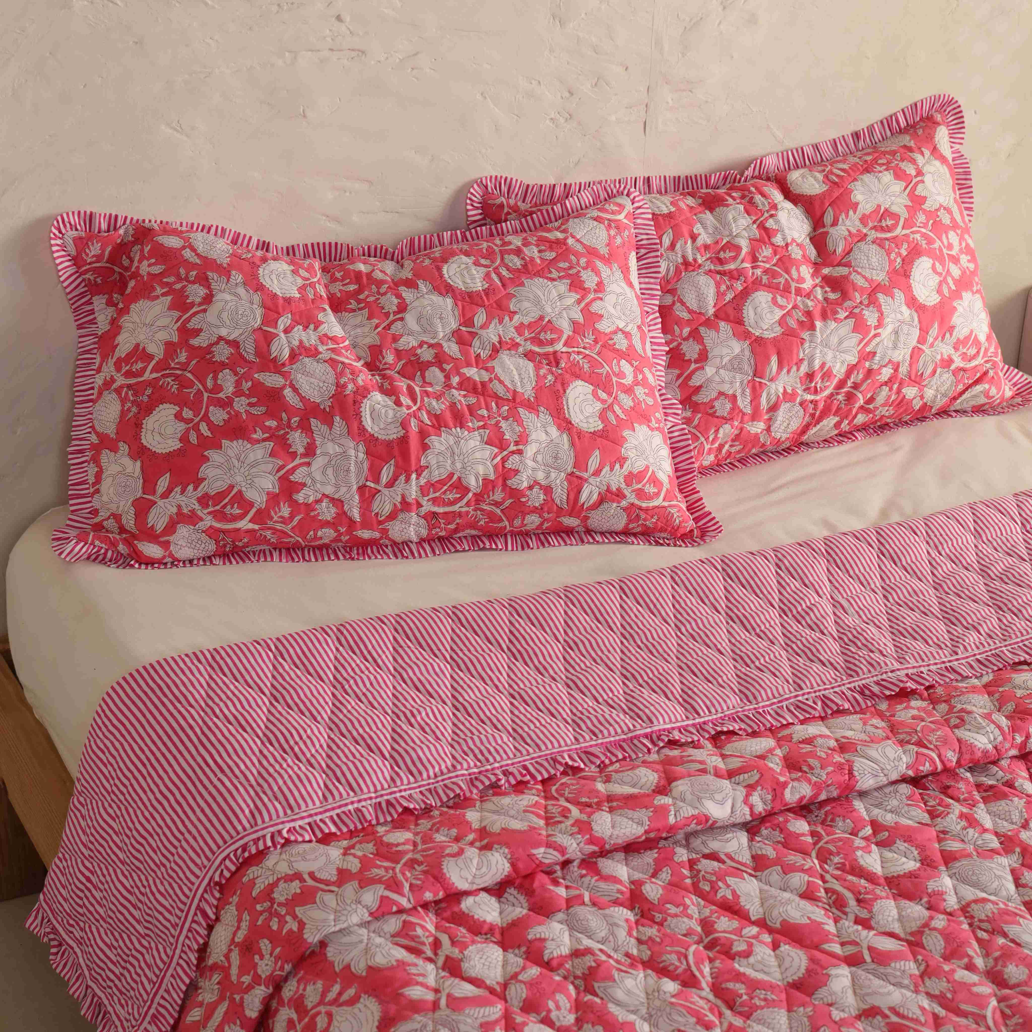 Pair of rose pink floral pillow covers with striped ruffle borders.