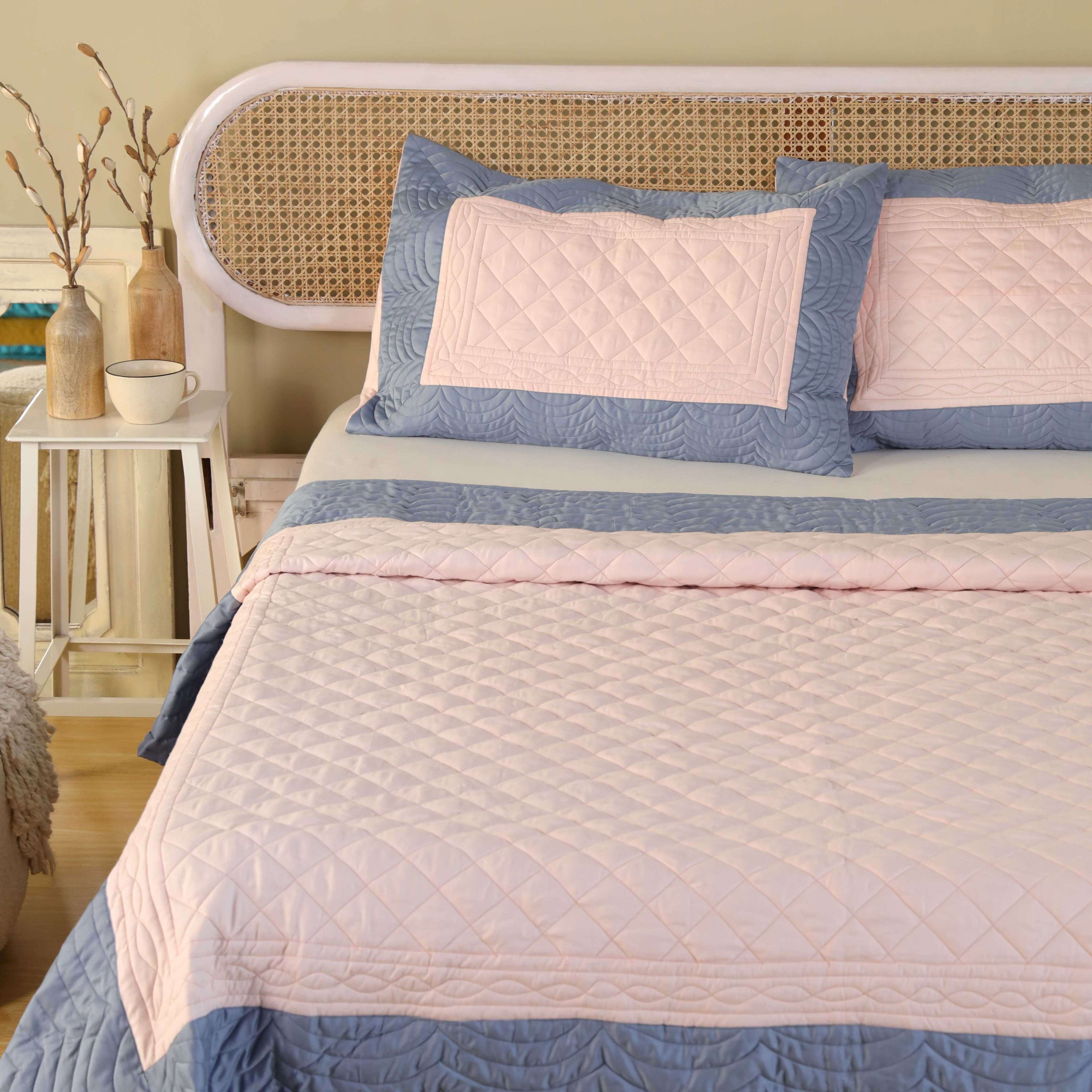 The scalloped blue edge and pink center of the satin quilt draped over a bed.