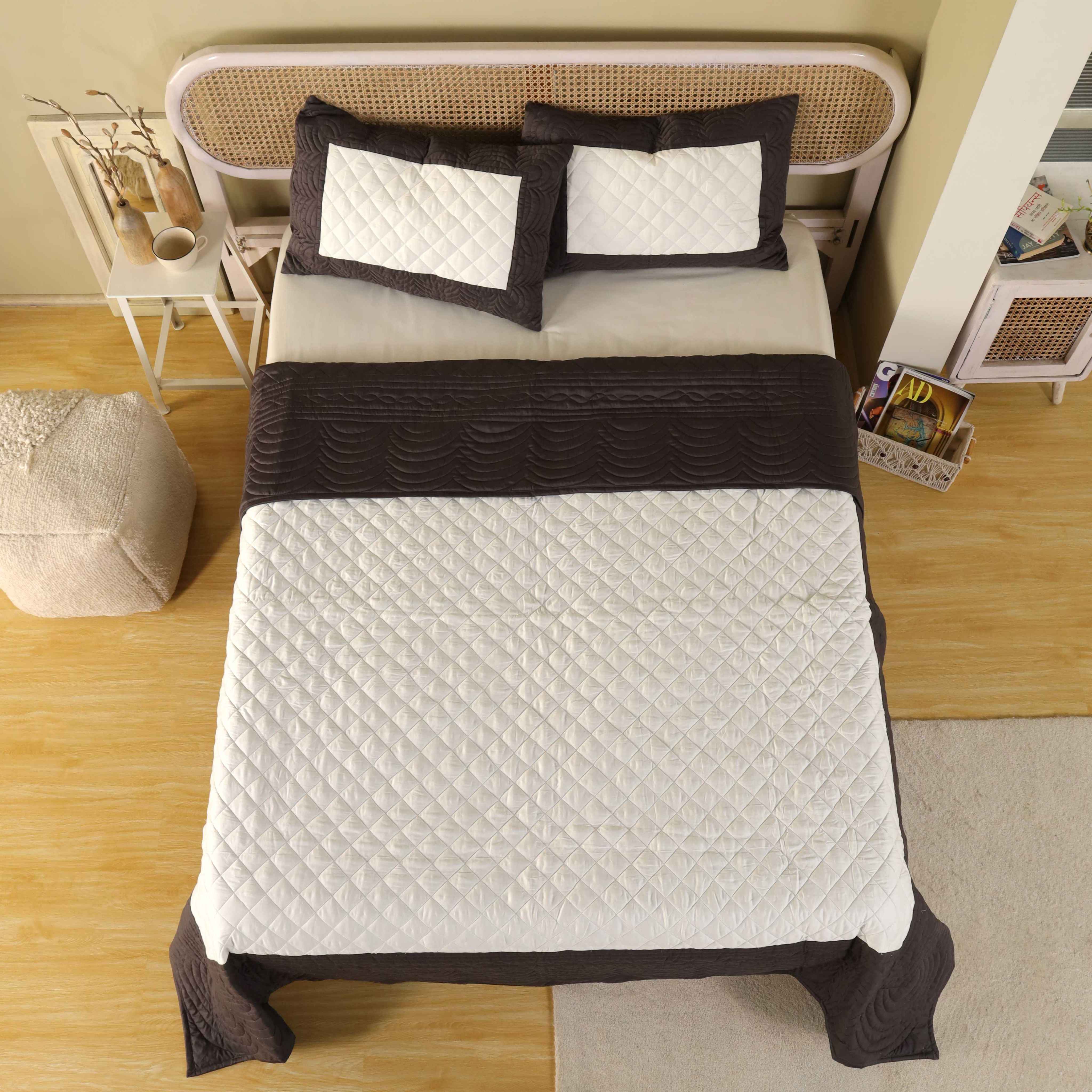The scalloped chocolate edge and white center of the satin quilt draped over a bed.