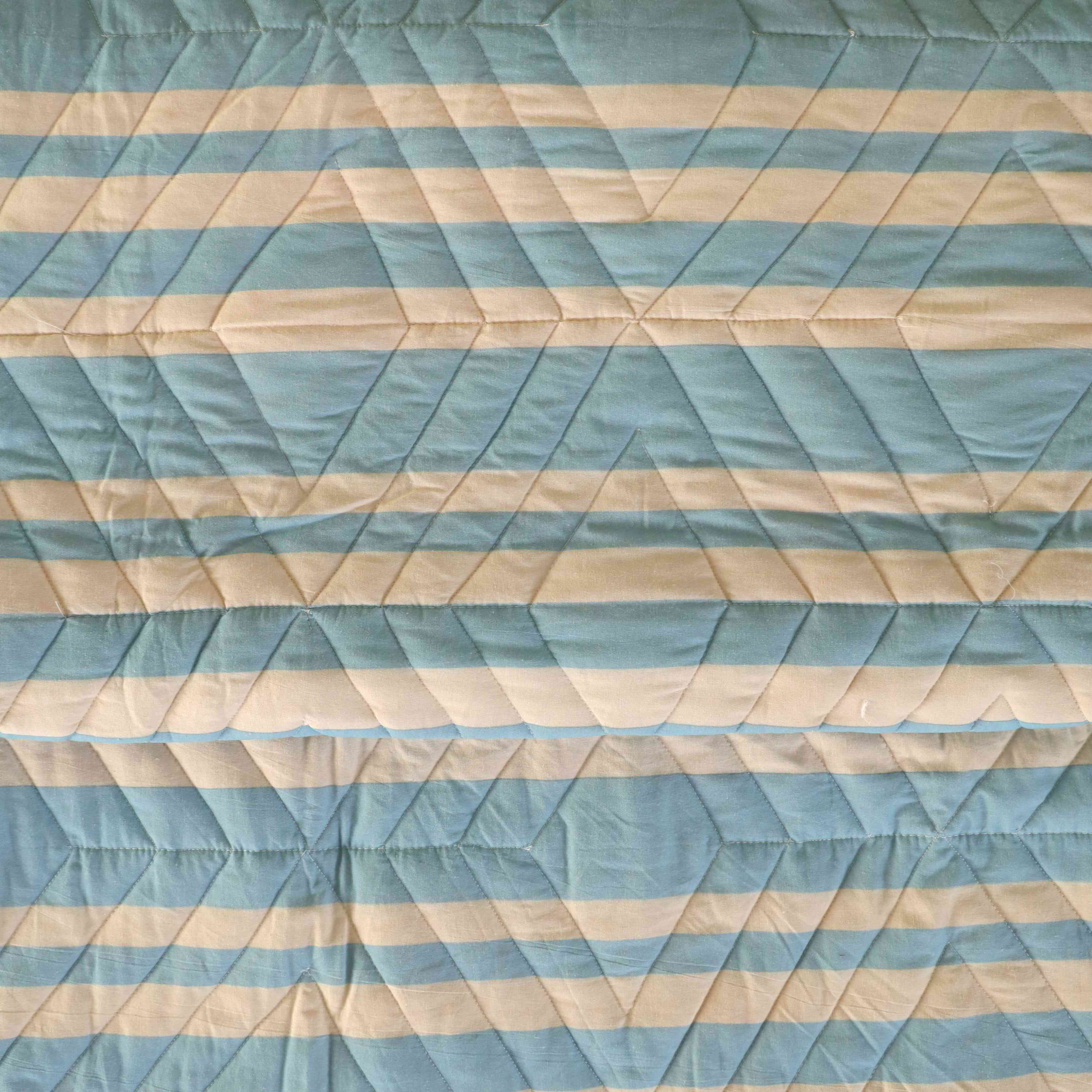 Two matching blue striped velvet pillow covers resting against a woven headboard.