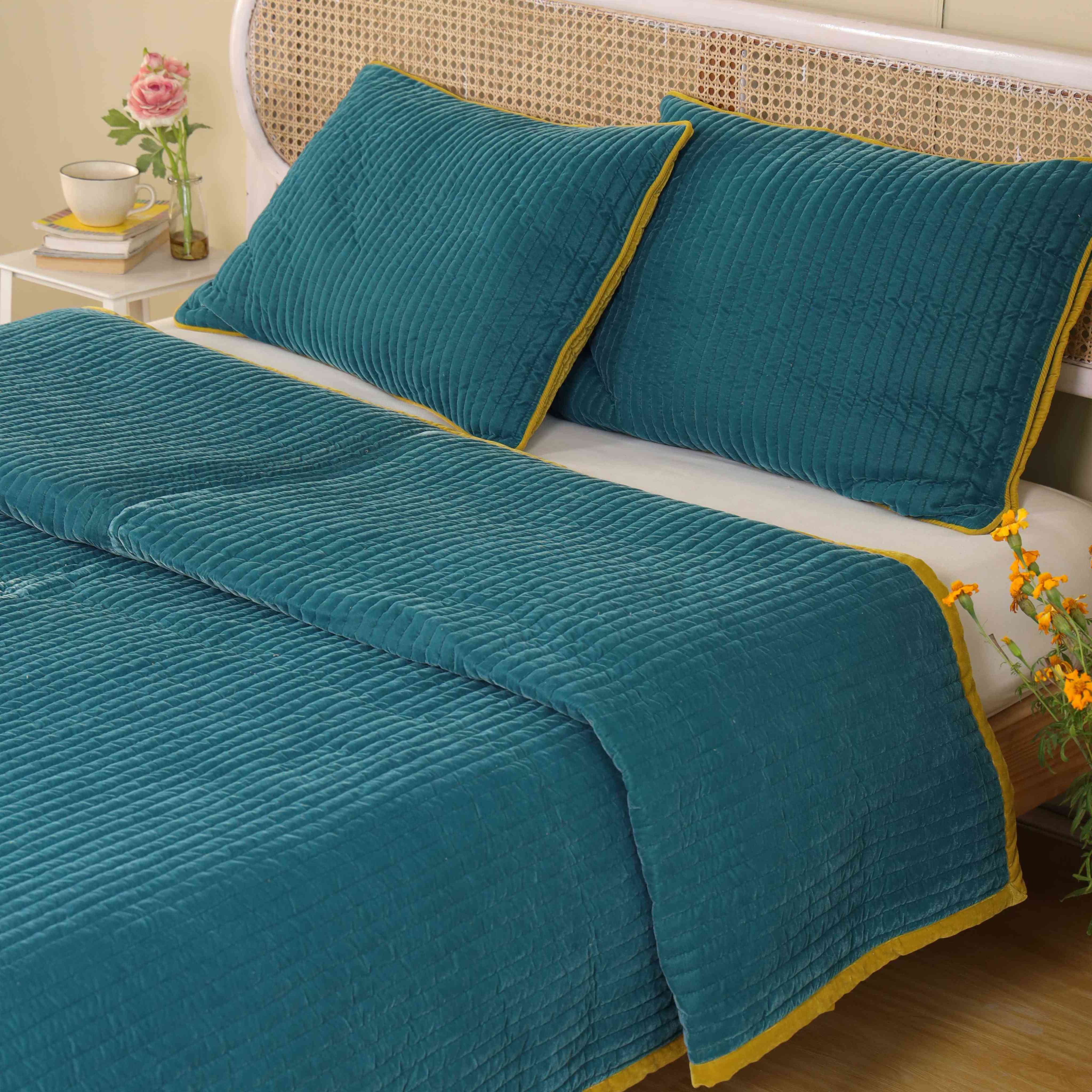 Close-up of two teal velvet pillow covers featuring mustard yellow piping and vertical channel stitching.
