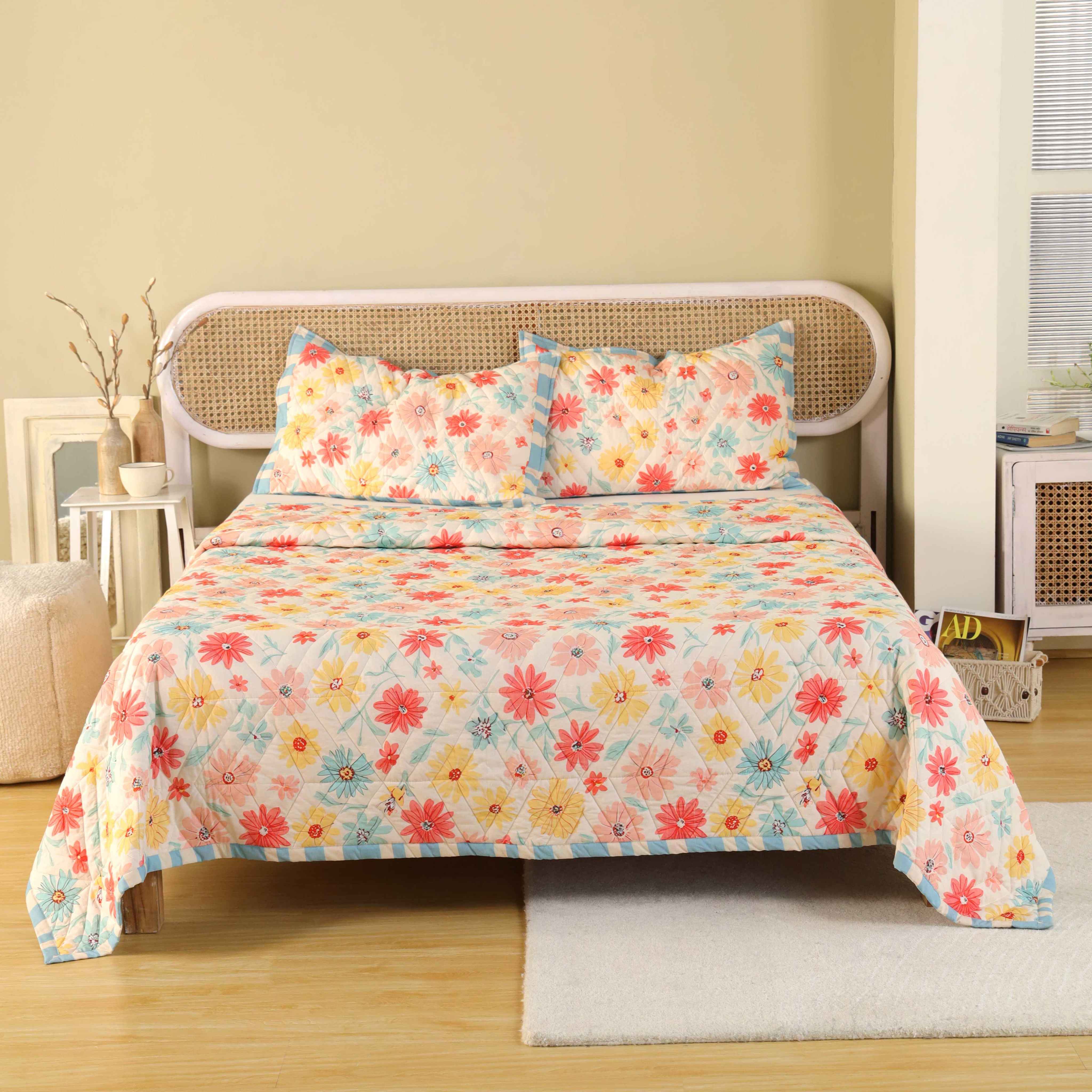 3-piece multi-color wildflower print cotton quilt set with blue striped ruffles on a bed.