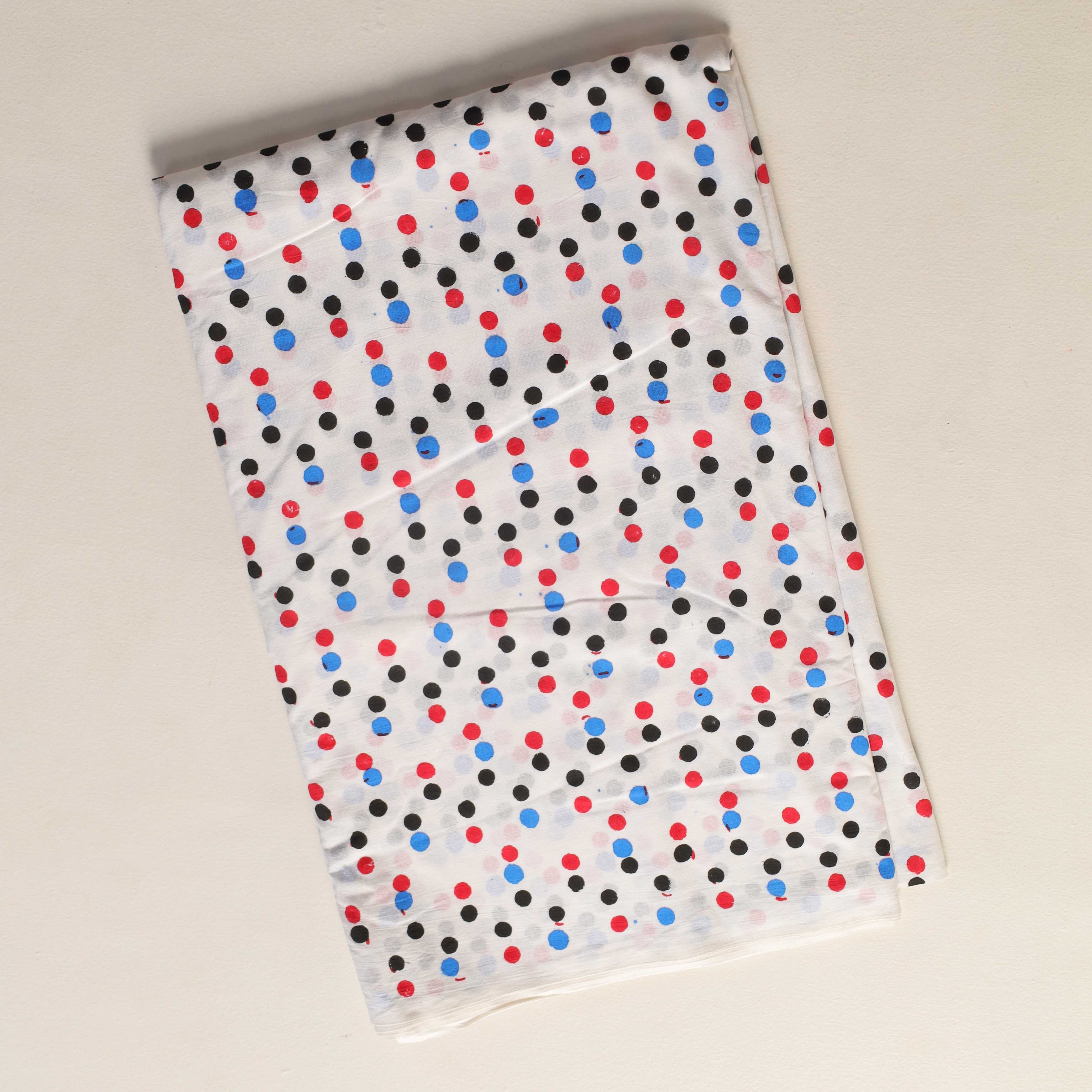 Folded fabric with red, blue, and black polka dot pattern on a beige background
