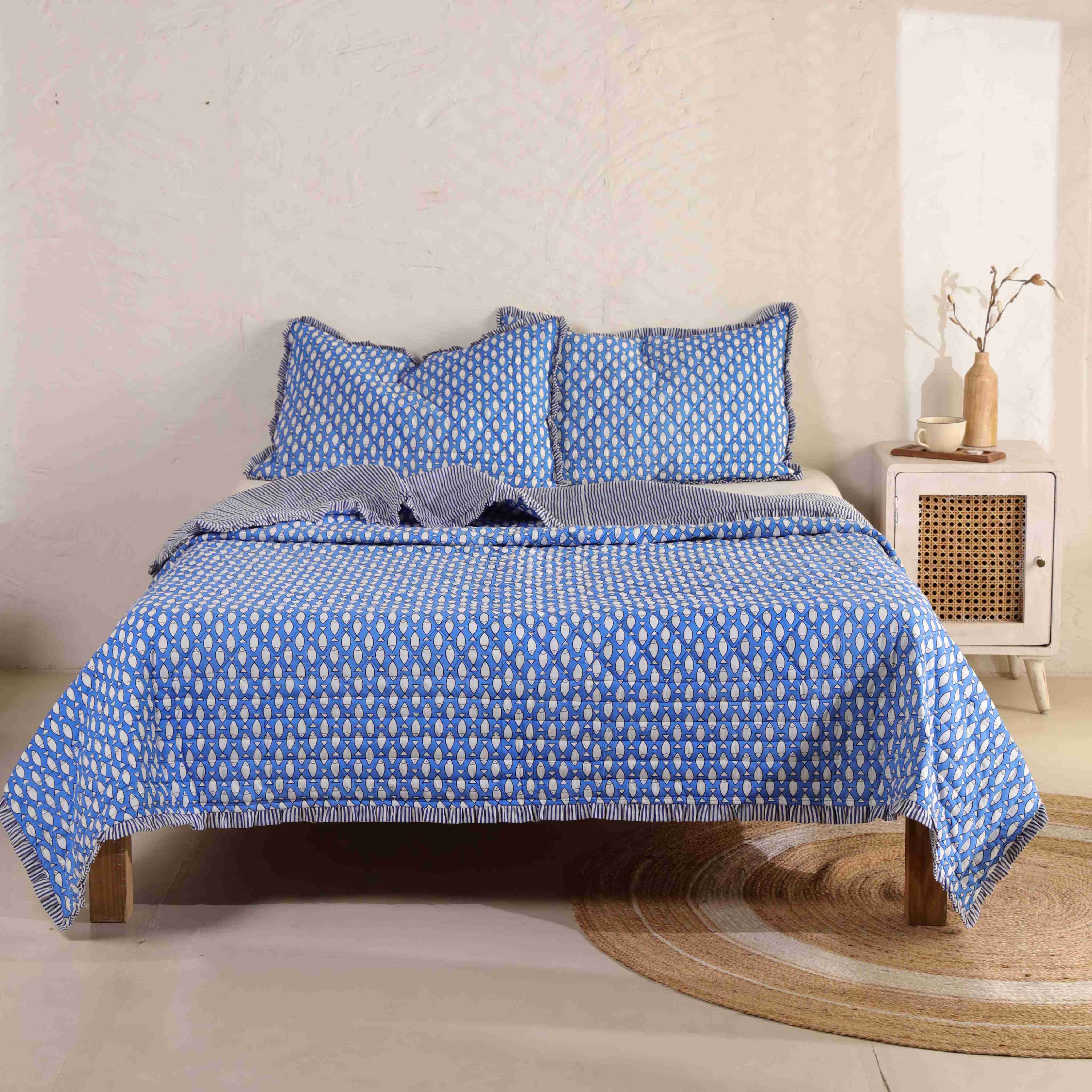 A 3-piece azure blue velvet quilt set with striped ruffle edges on a wooden bed.