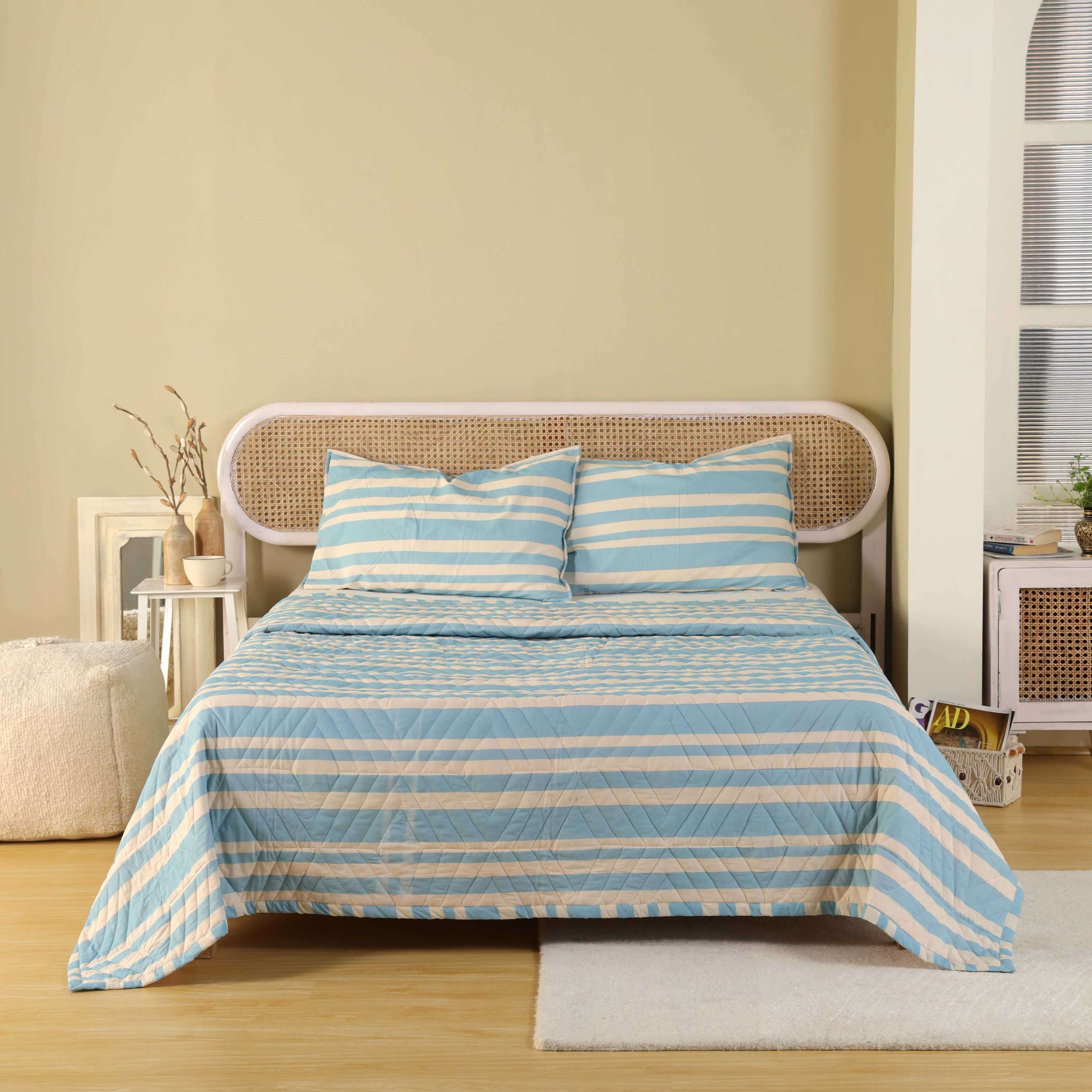 A modern blue and cream striped velvet quilt set on a bed with a rattan headboard.