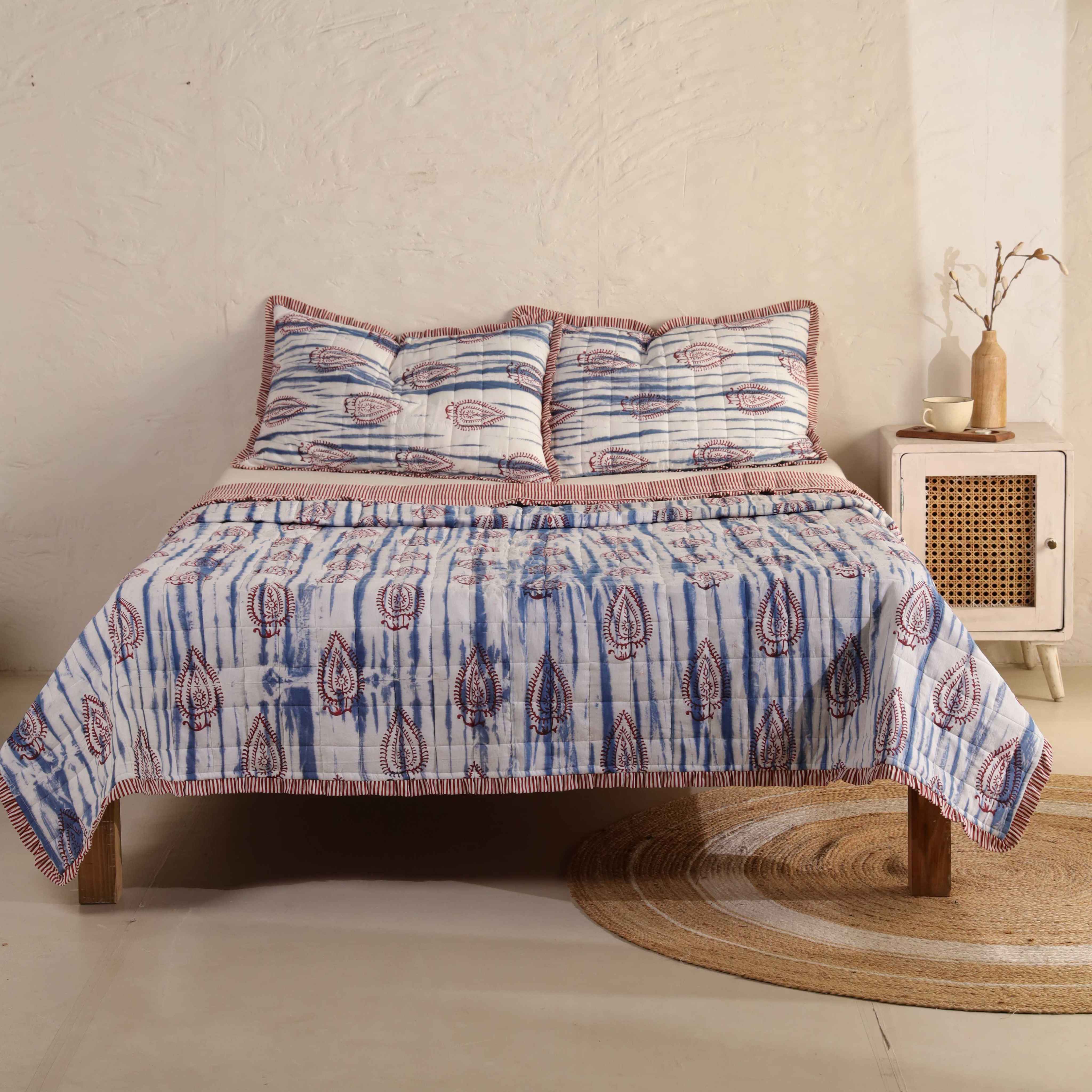 3-piece blue and white boho cotton quilt set with striped ruffle edges on a wooden bed.