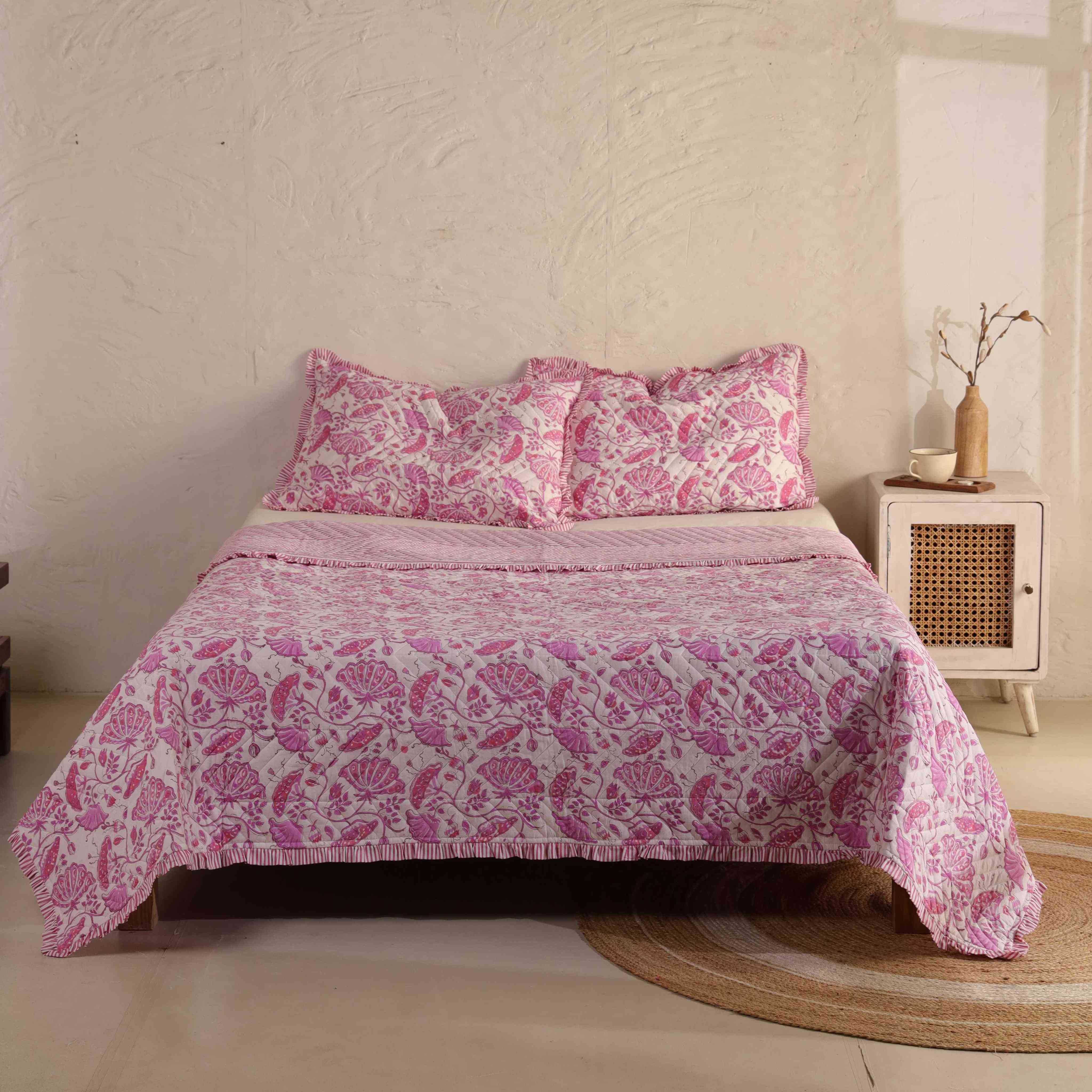 3-piece blush pink floral velvet quilt set with striped ruffle edges on a bed.