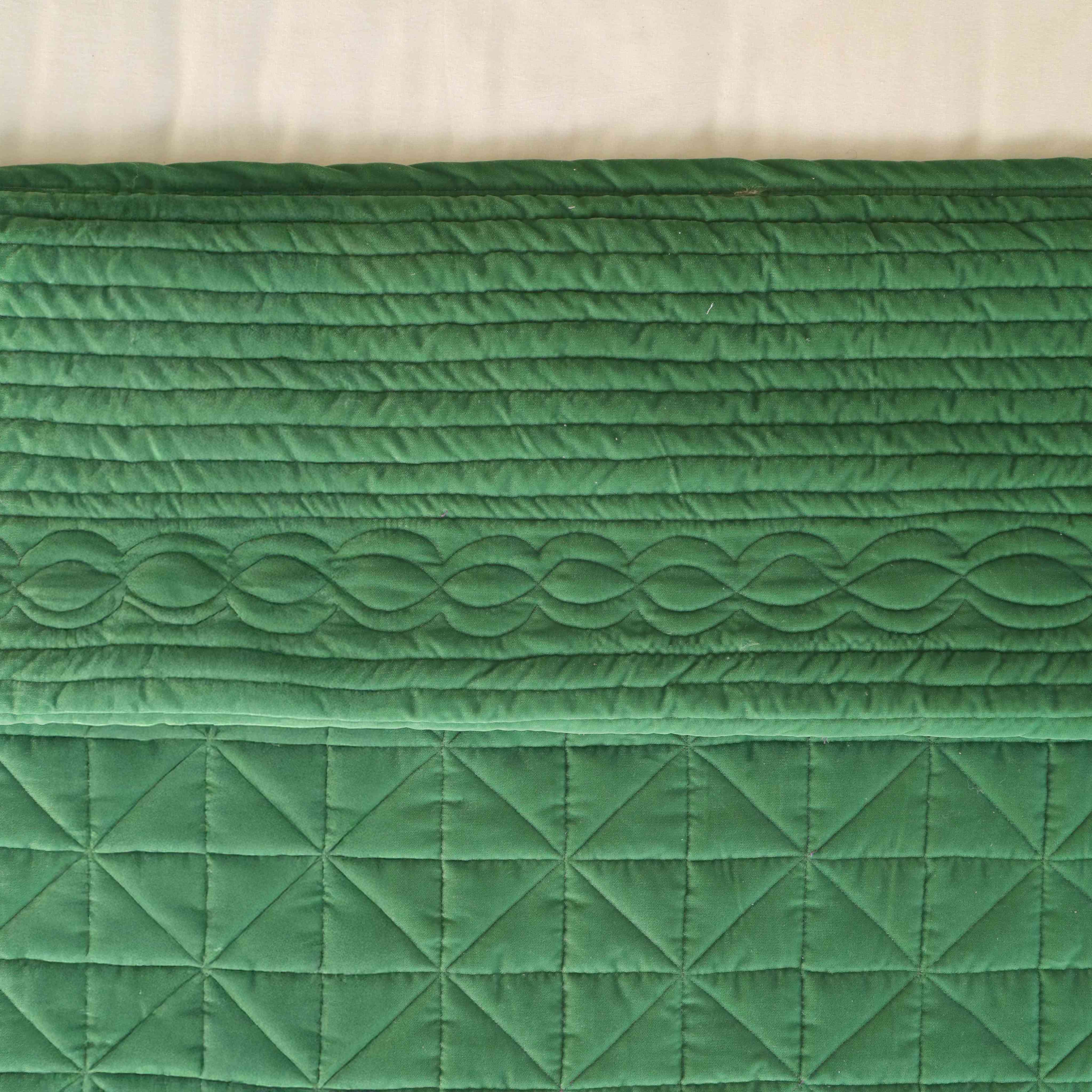 Detailed close-up of the silky satin fabric and multi-pattern quilted texture in emerald green