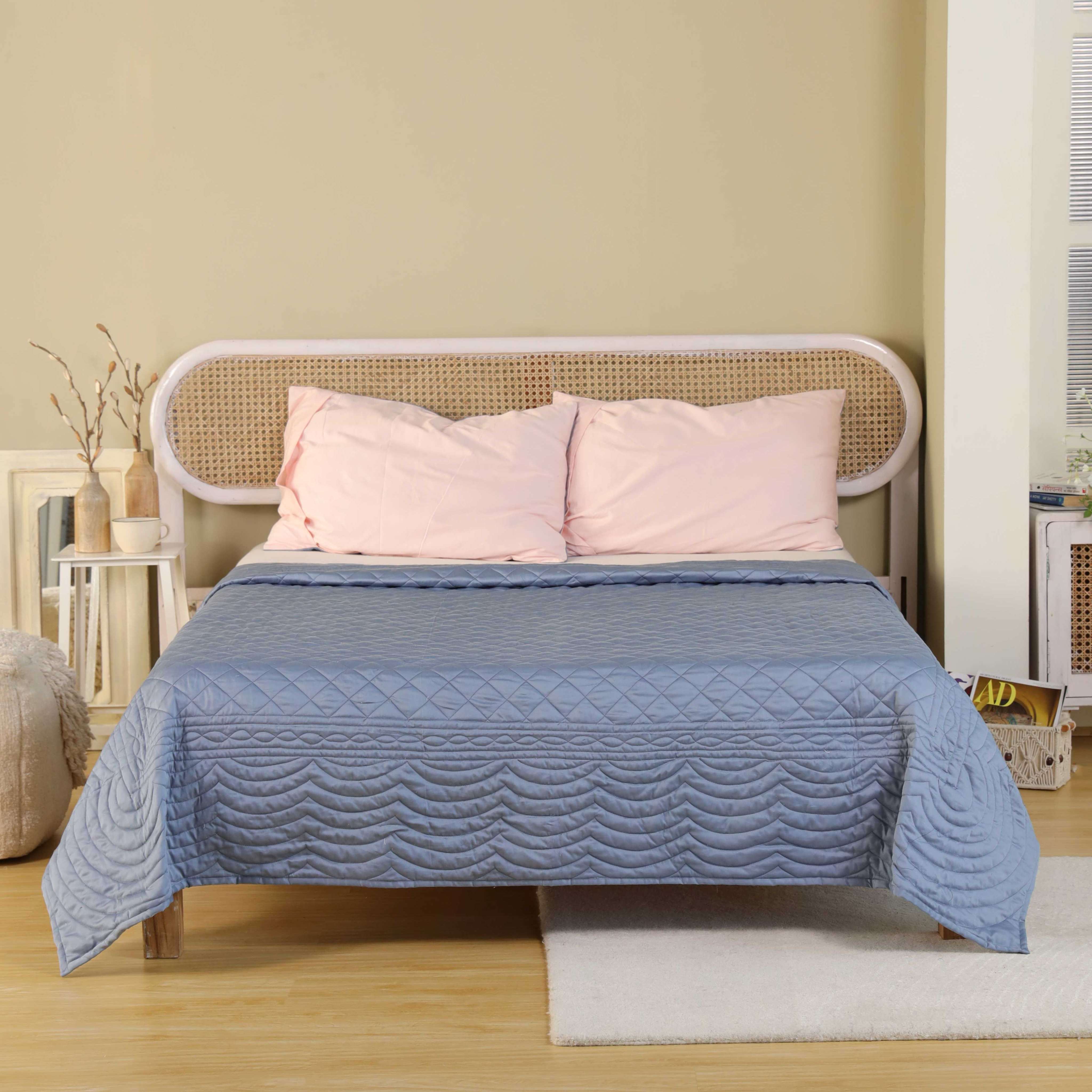 A dusty blue satin quilt with scalloped wave borders and plain pink pillows.