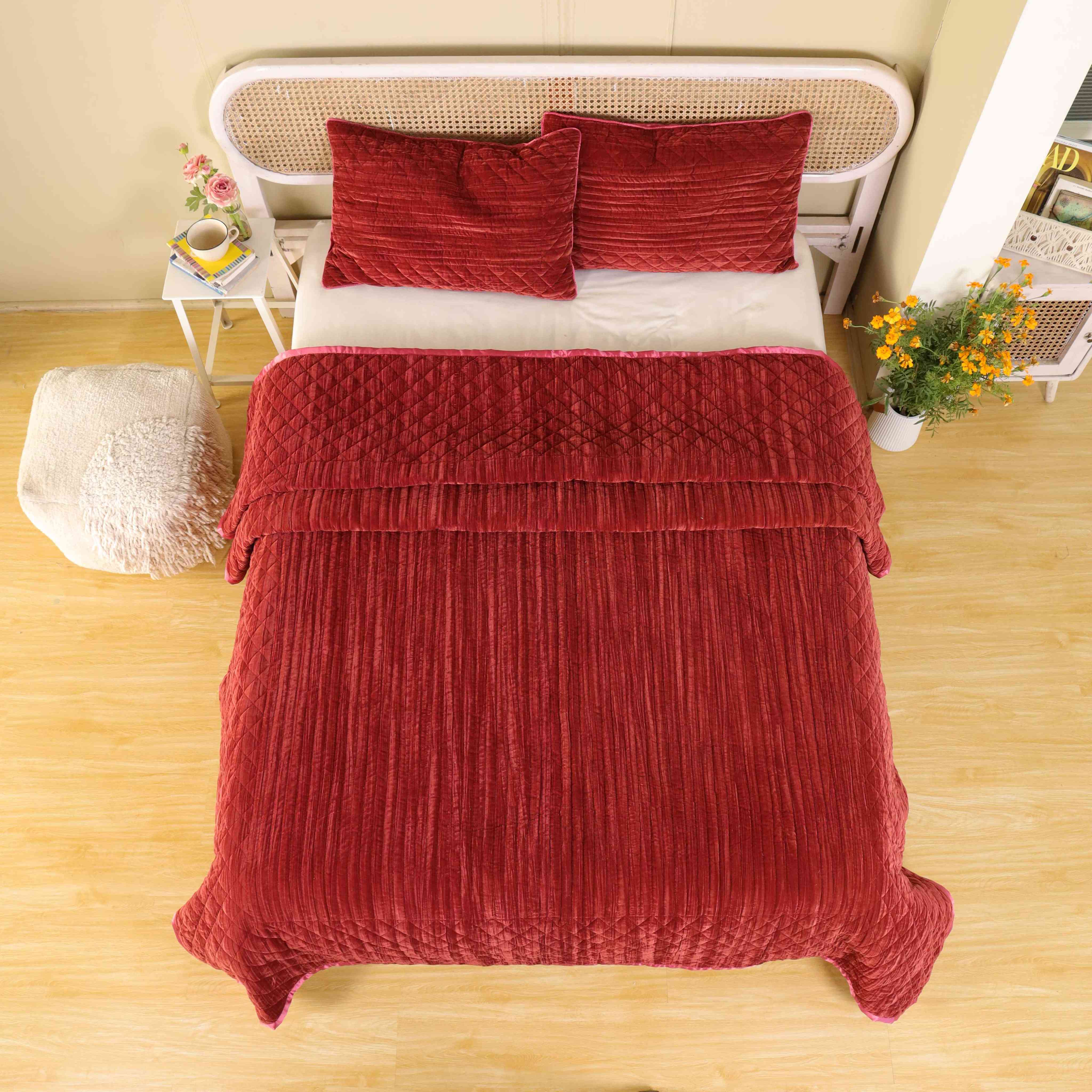 Faded maroon velvet quilt set on a bed with a rattan headboard in a bright room.