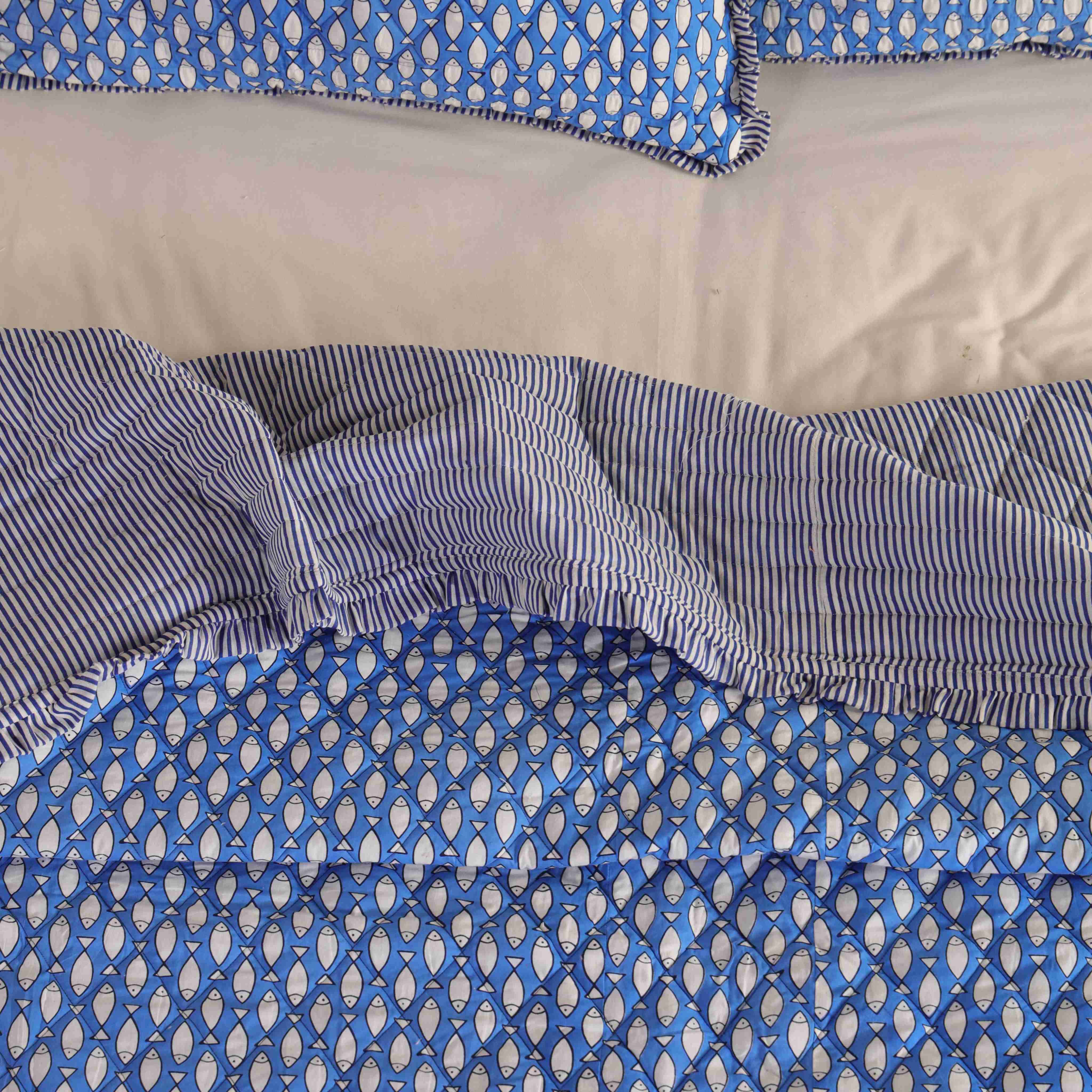 Neatly folded azure blue velvet quilt set showing the plushness and striped ruffle detail.