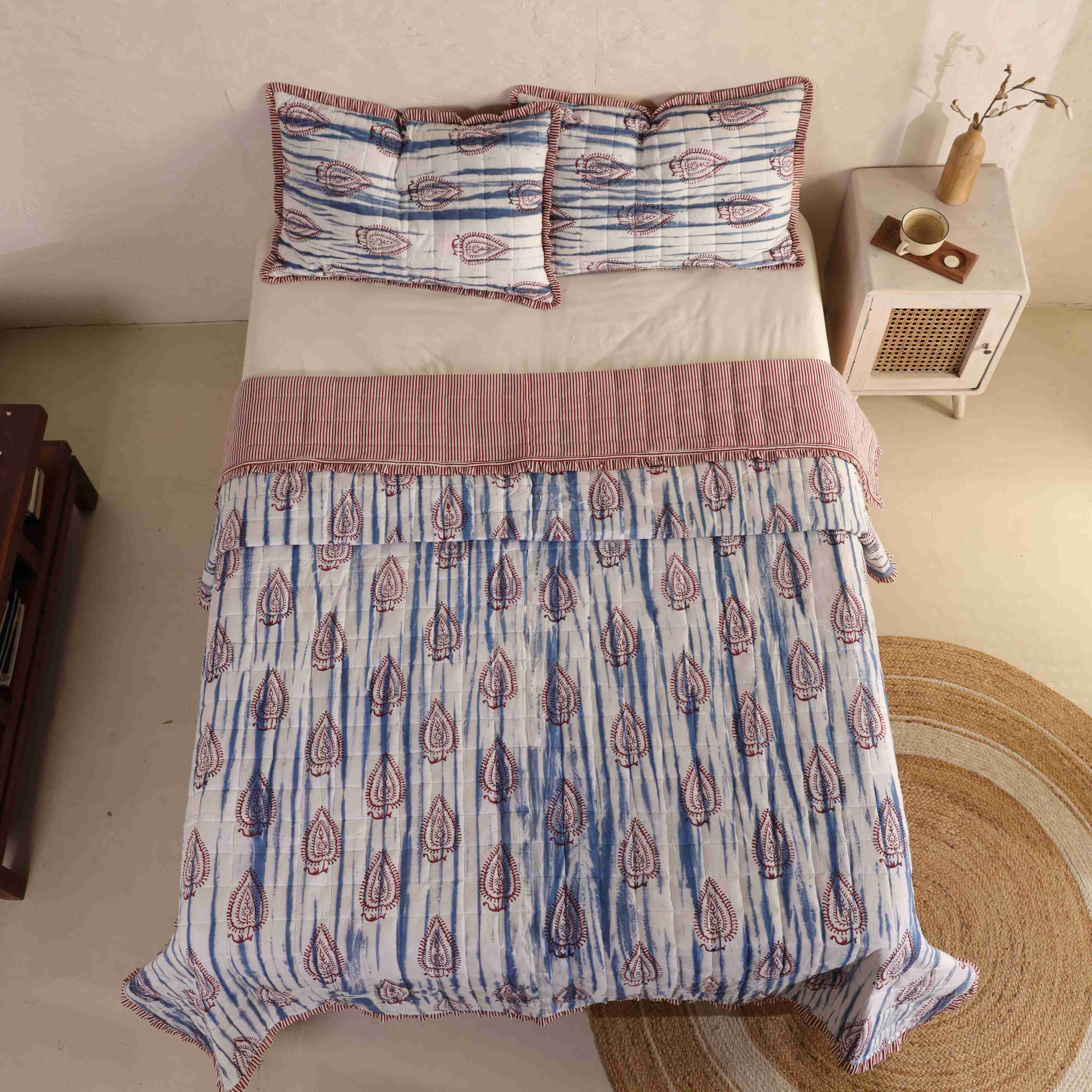 A neatly folded blue and white cotton quilt set showing the stitching and striped ruffle detail.