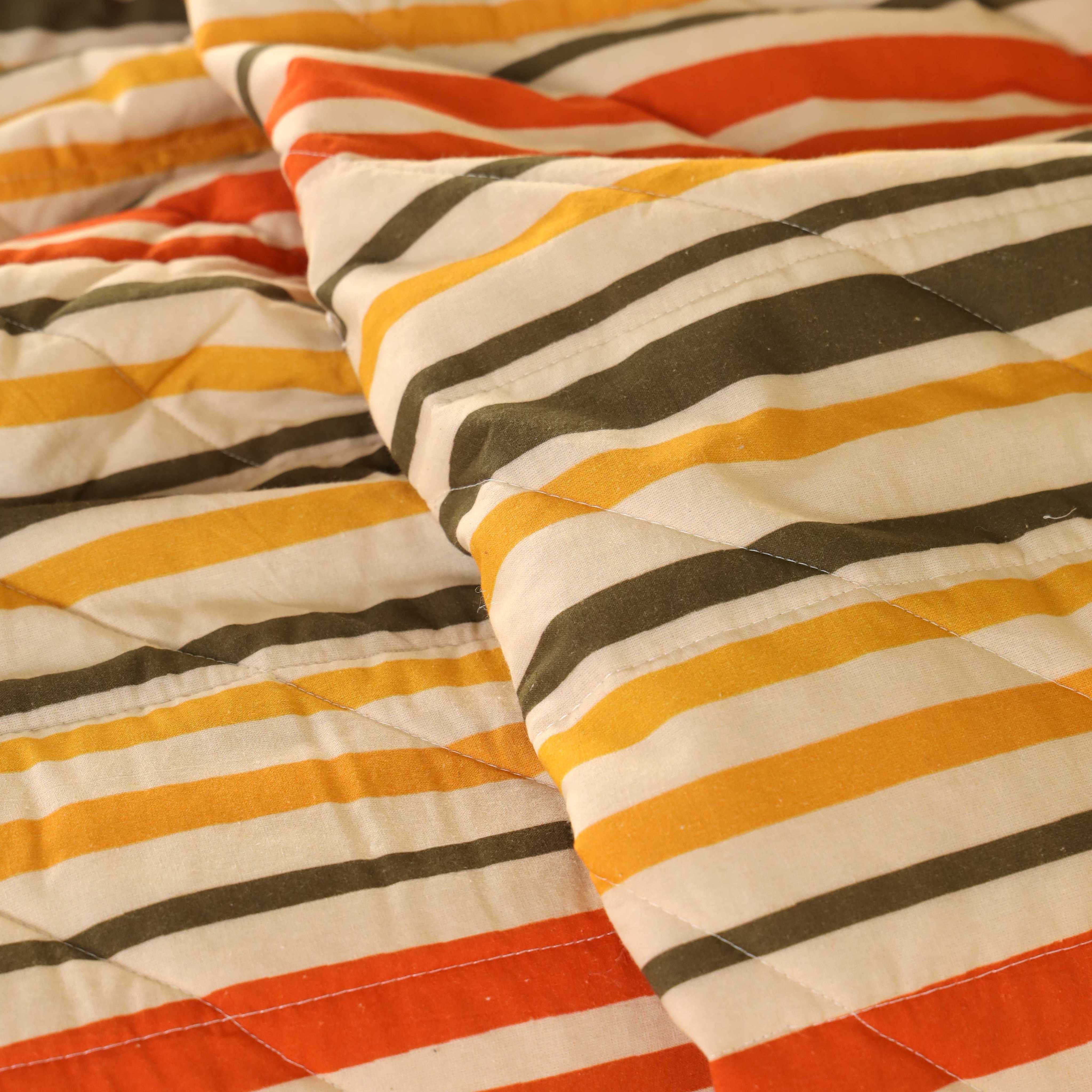 A neatly folded sunset stripe cotton quilt set showing its plushness and earthy colors.