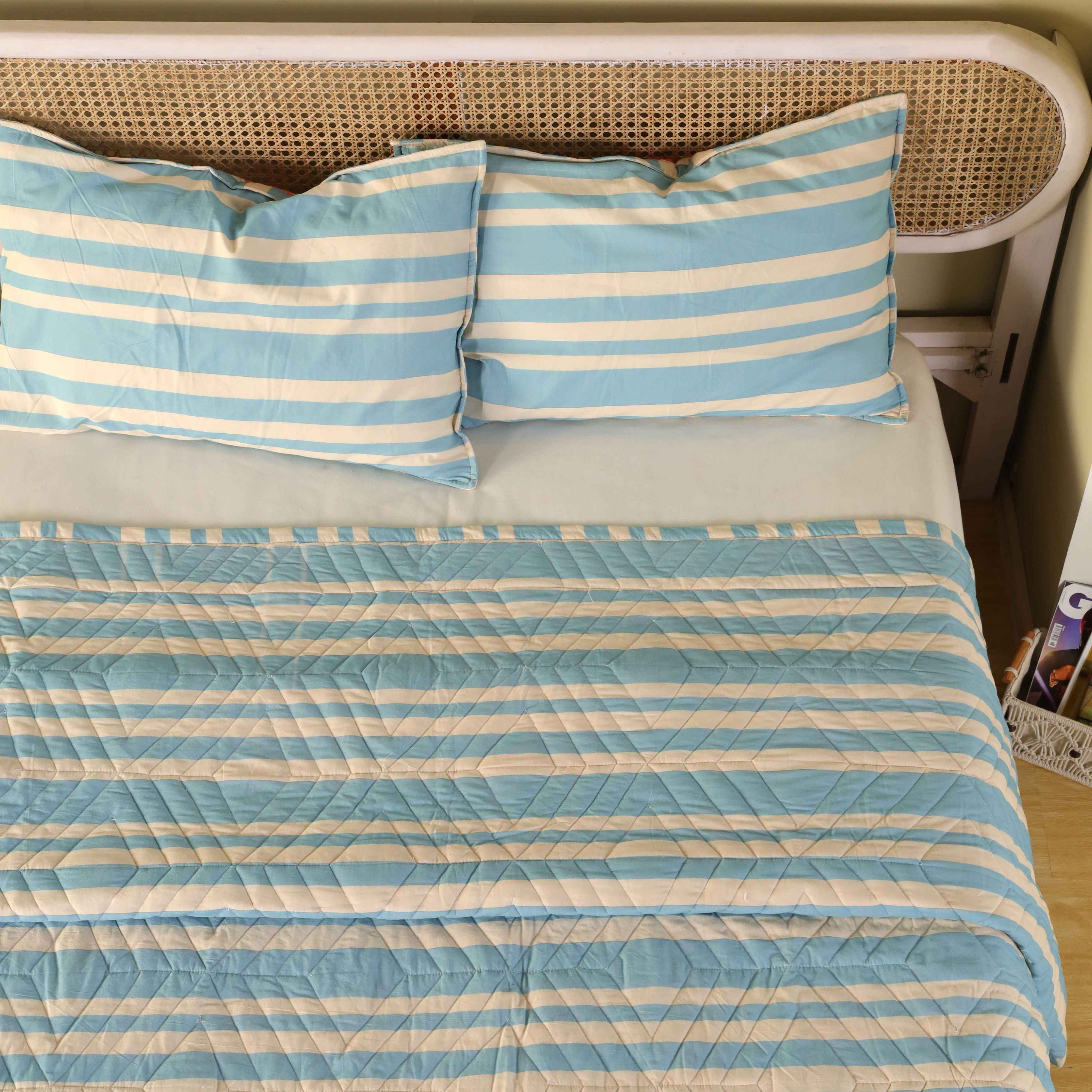 The blue striped velvet quilt draped over the foot of the bed showing its drape and thickness.