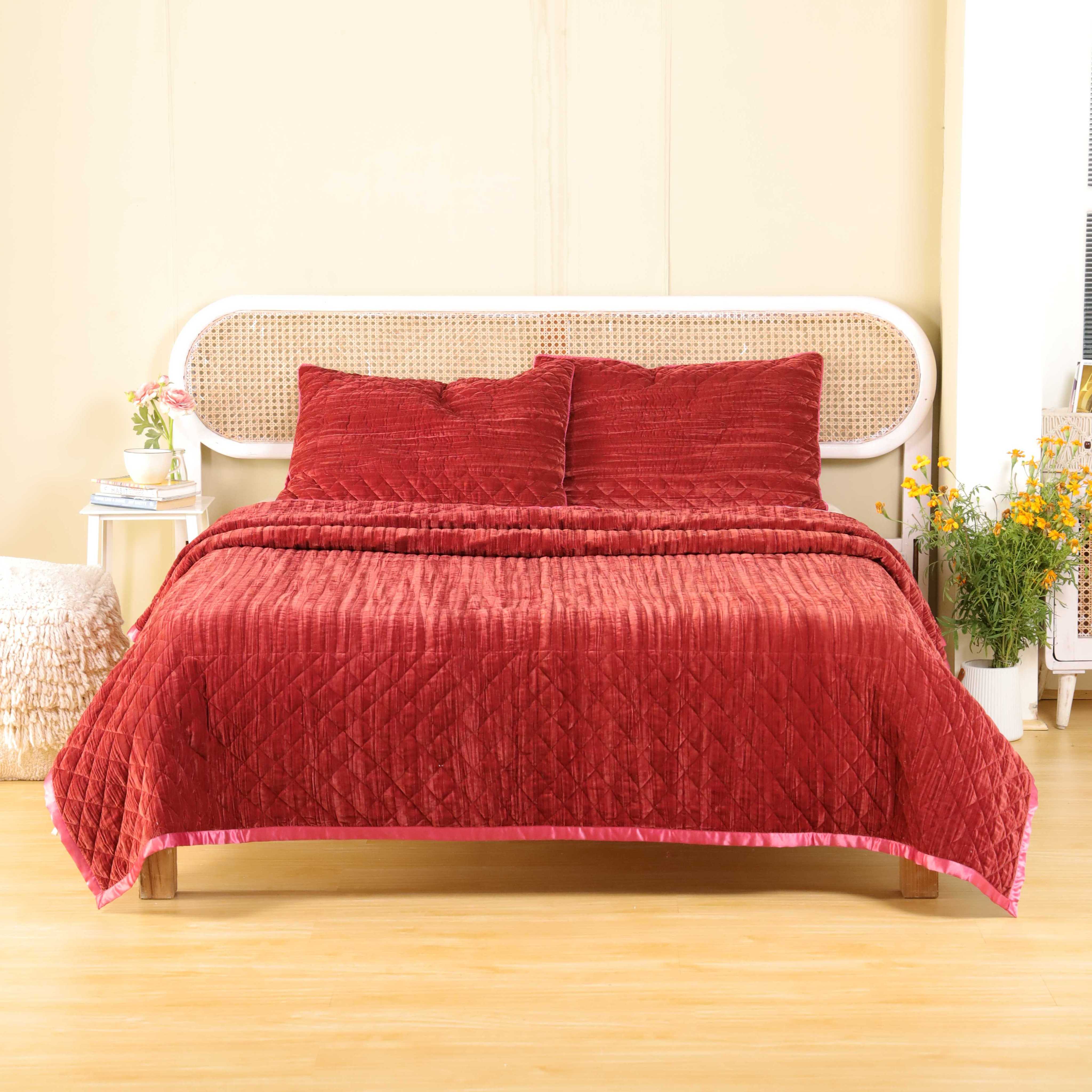 Overhead view of a modern bedroom styled with a rich faded maroon velvet quilt and neutral decor.