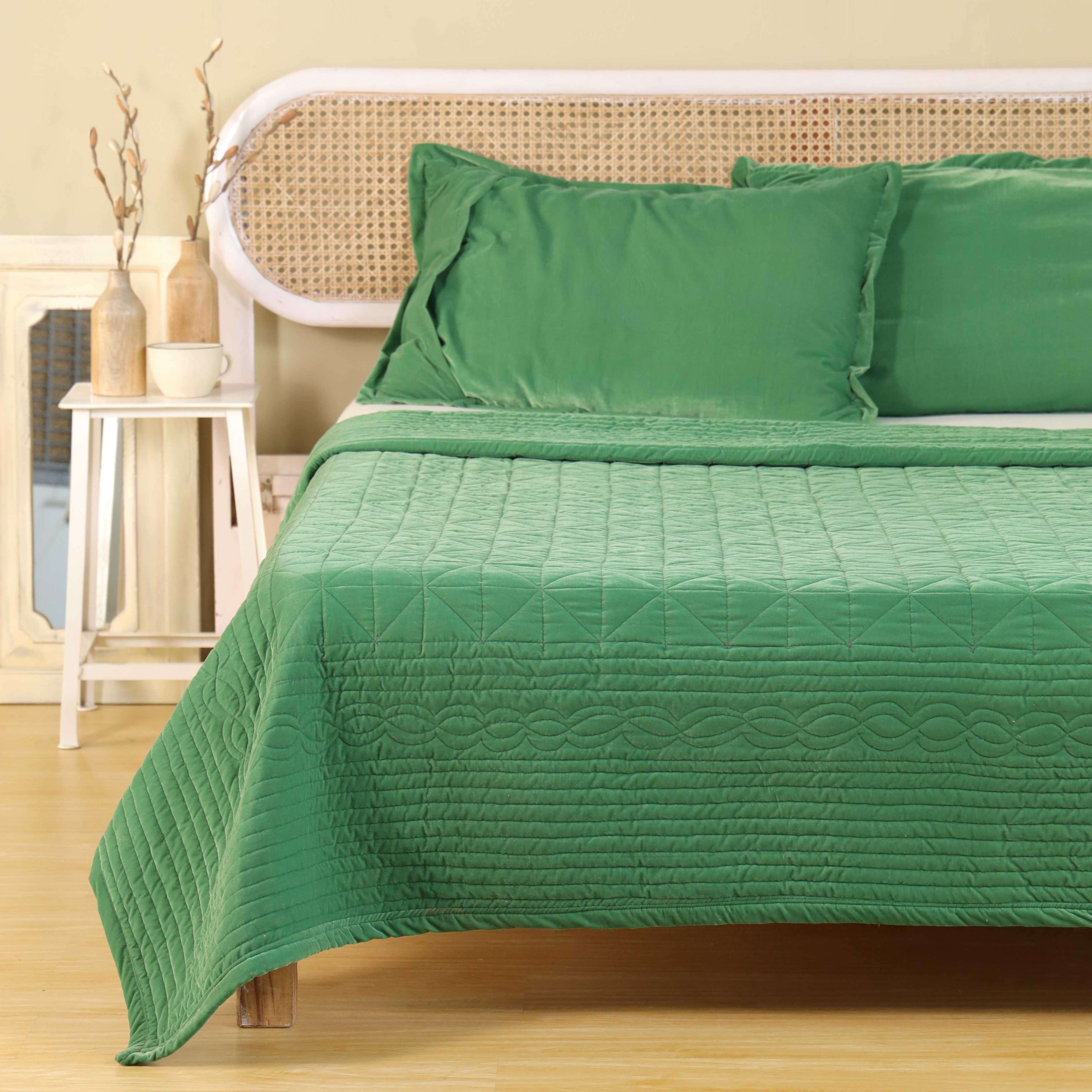 Luxury emerald green satin bedding set styled in a bright minimalist bedroom with a cane headboard.