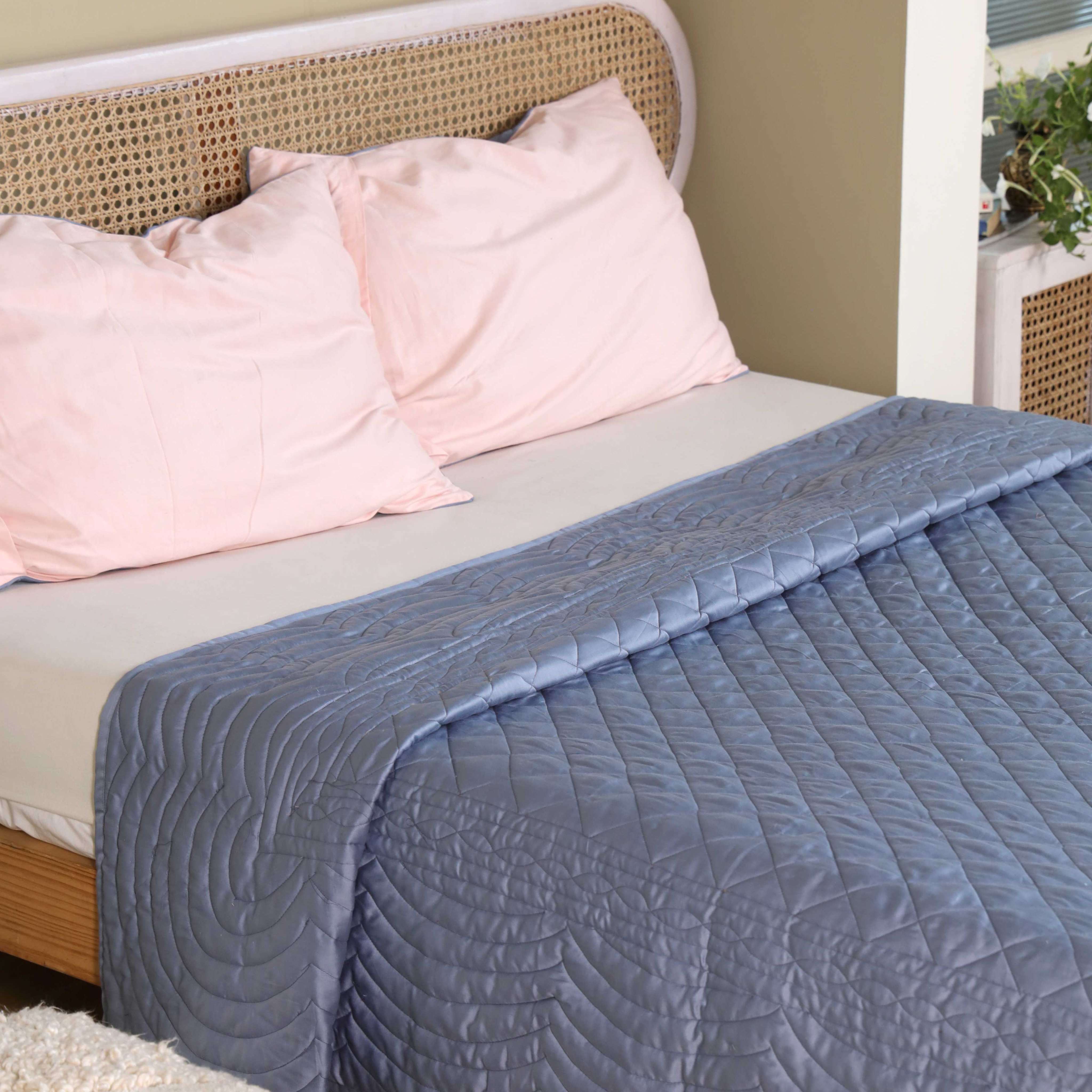 The center diamond quilting and scalloped edge of a blue satin quilt.