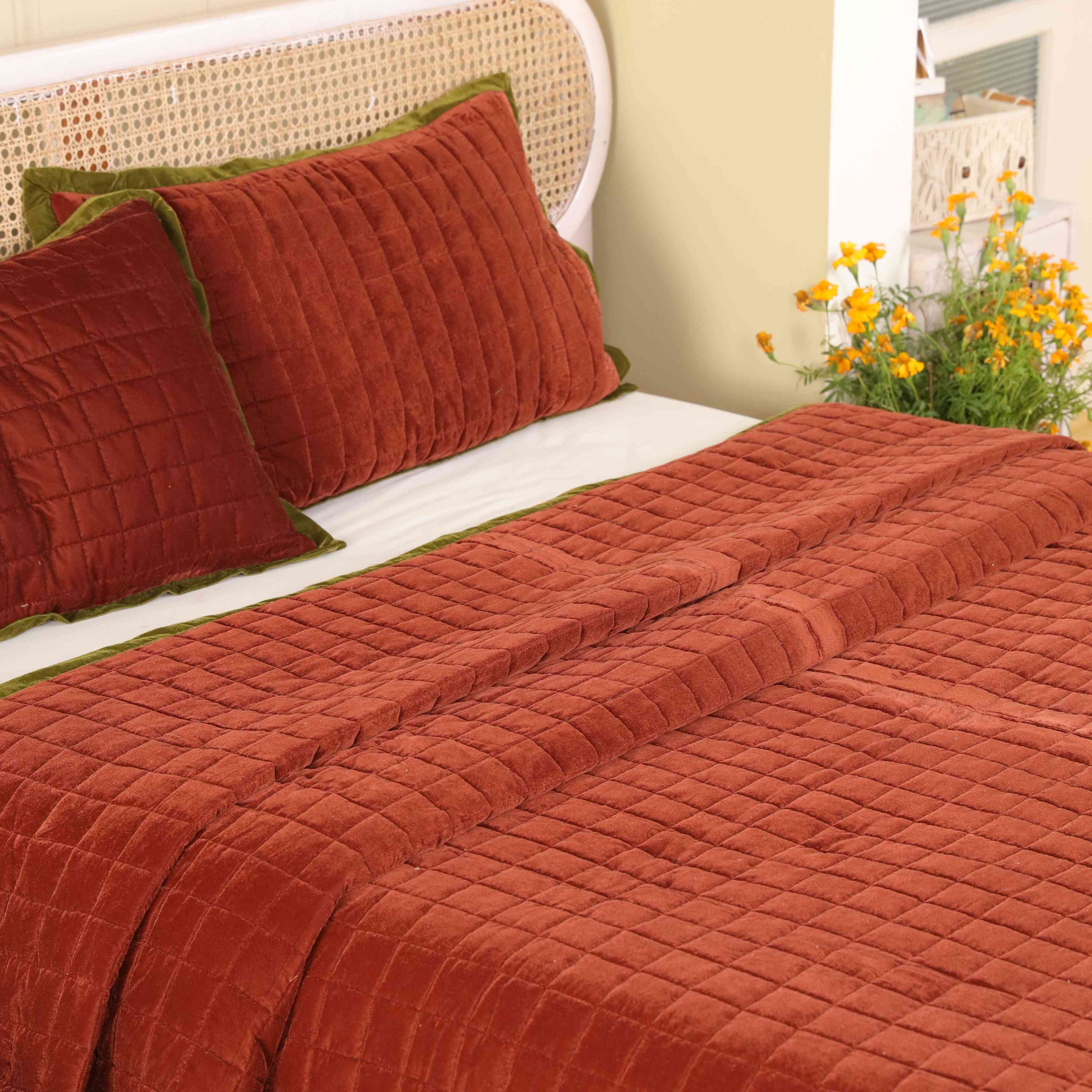 Close-up of two faded maroon velvet pillow covers featuring box-stitch quilting and green piping.