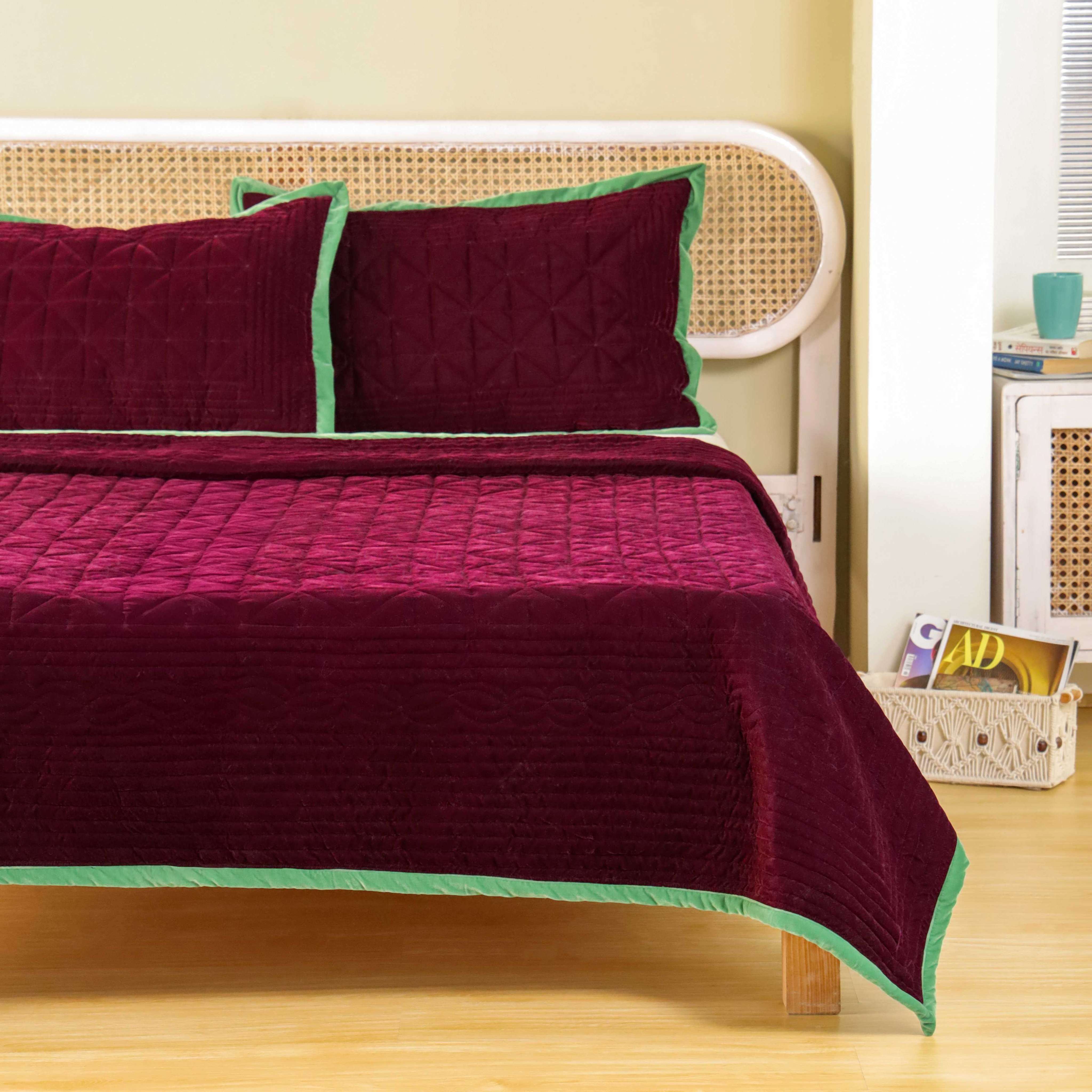 Two maroon velvet pillow covers featuring vertical and diamond quilting with green piping.