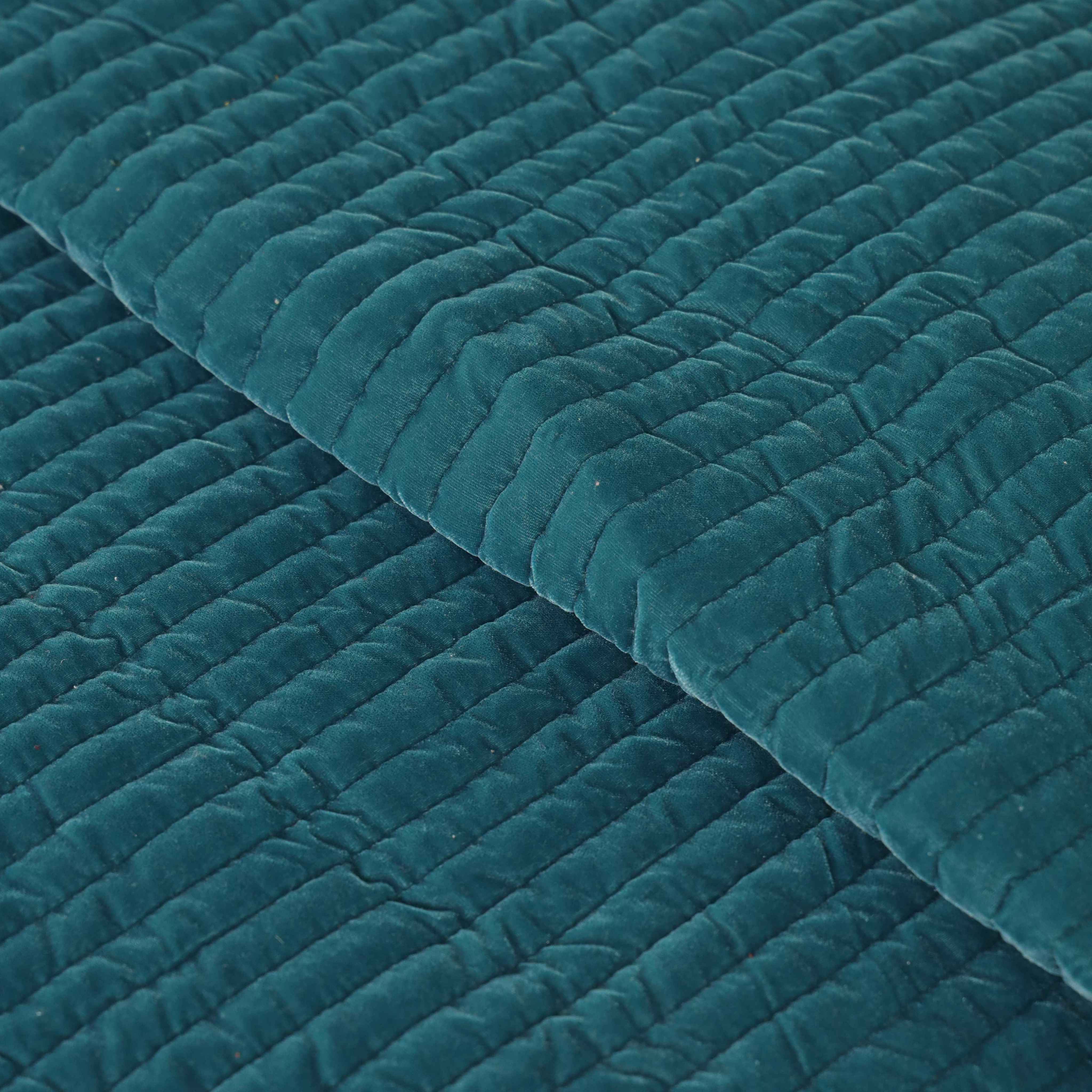High-angle view of a cozy teal and mustard velvet bedding set in a minimalist home setting.