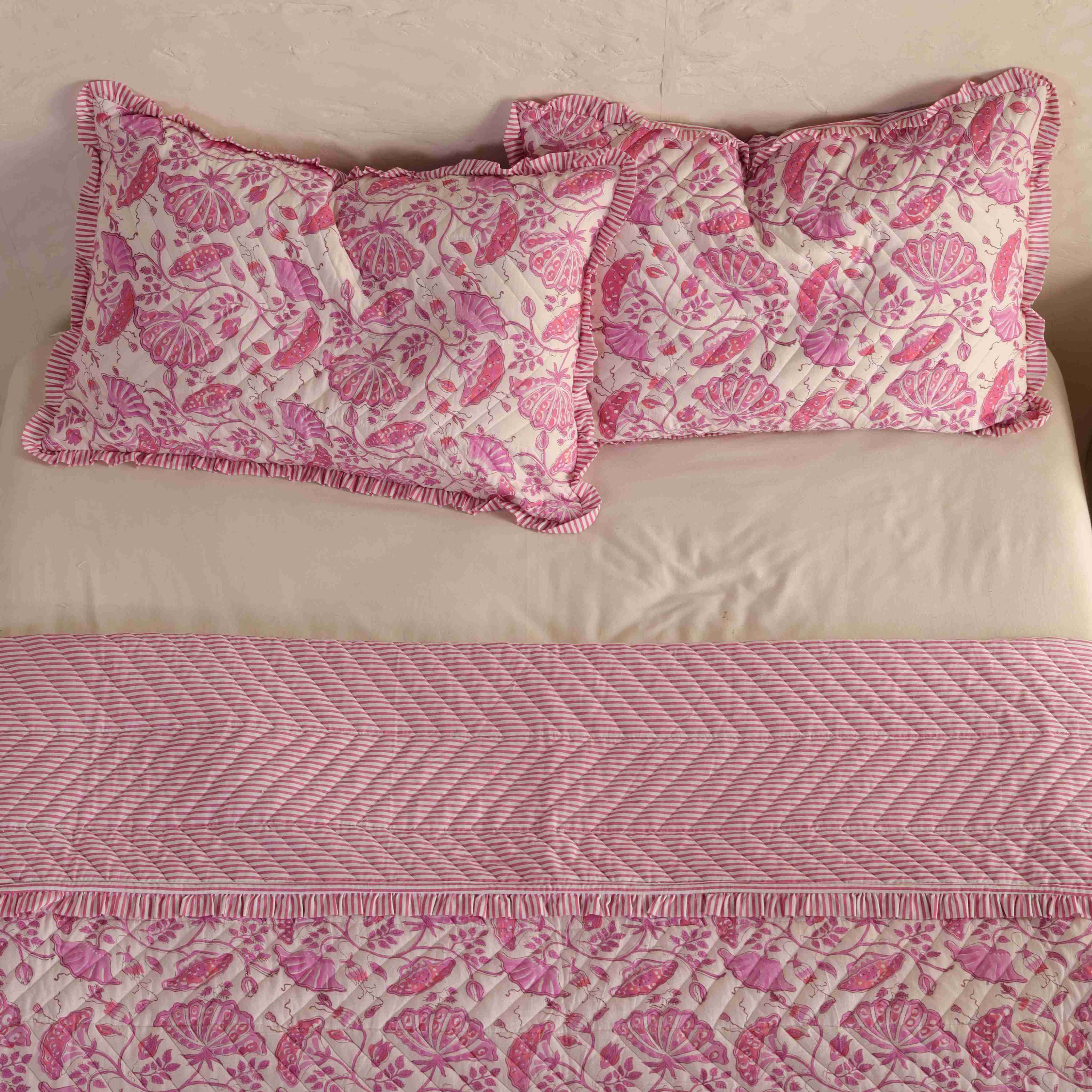 Shabby chic bedroom interior featuring a pink velvet floral quilt and white nightstand.