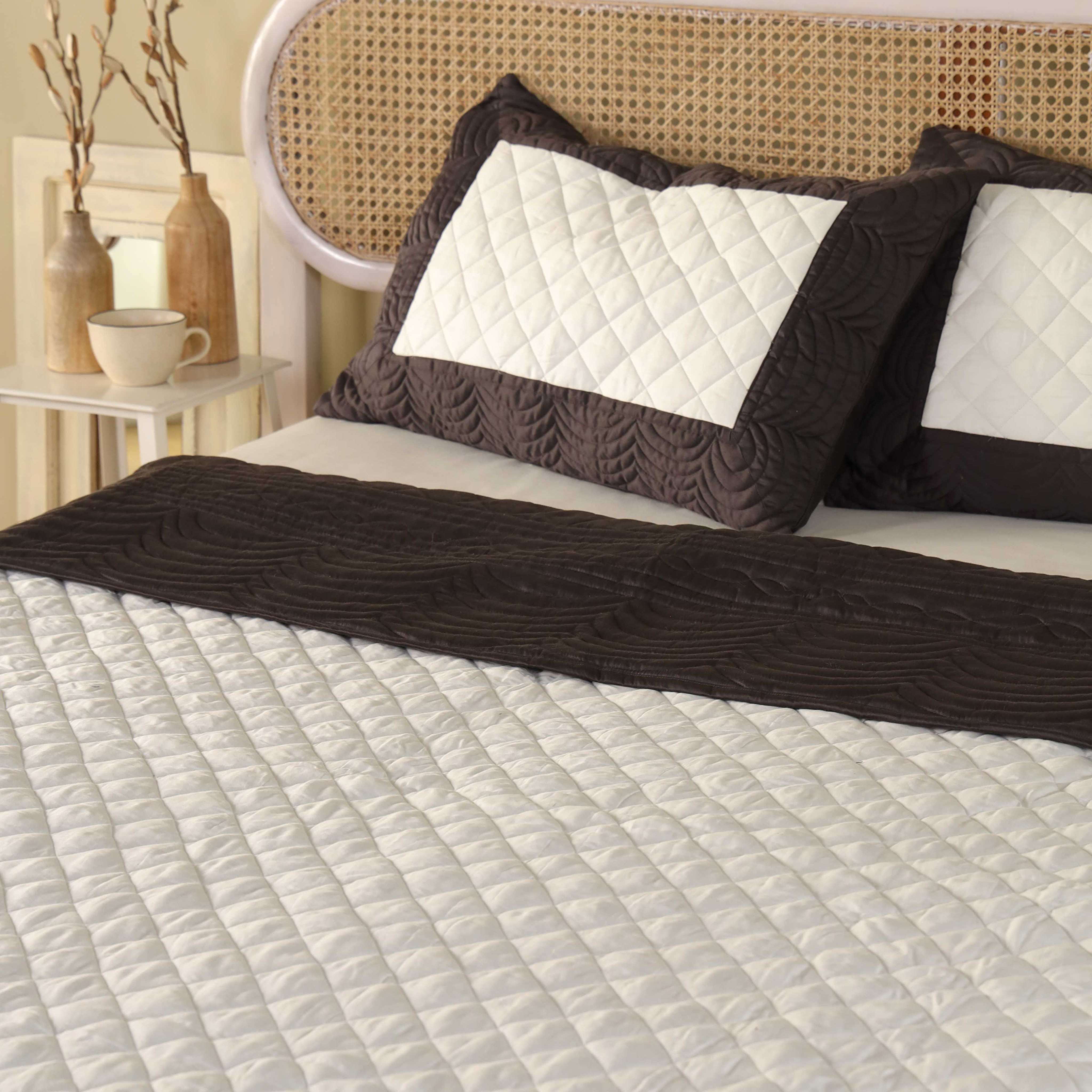A styled master bedroom featuring a chocolate and white satin quilt with minimalist decor.