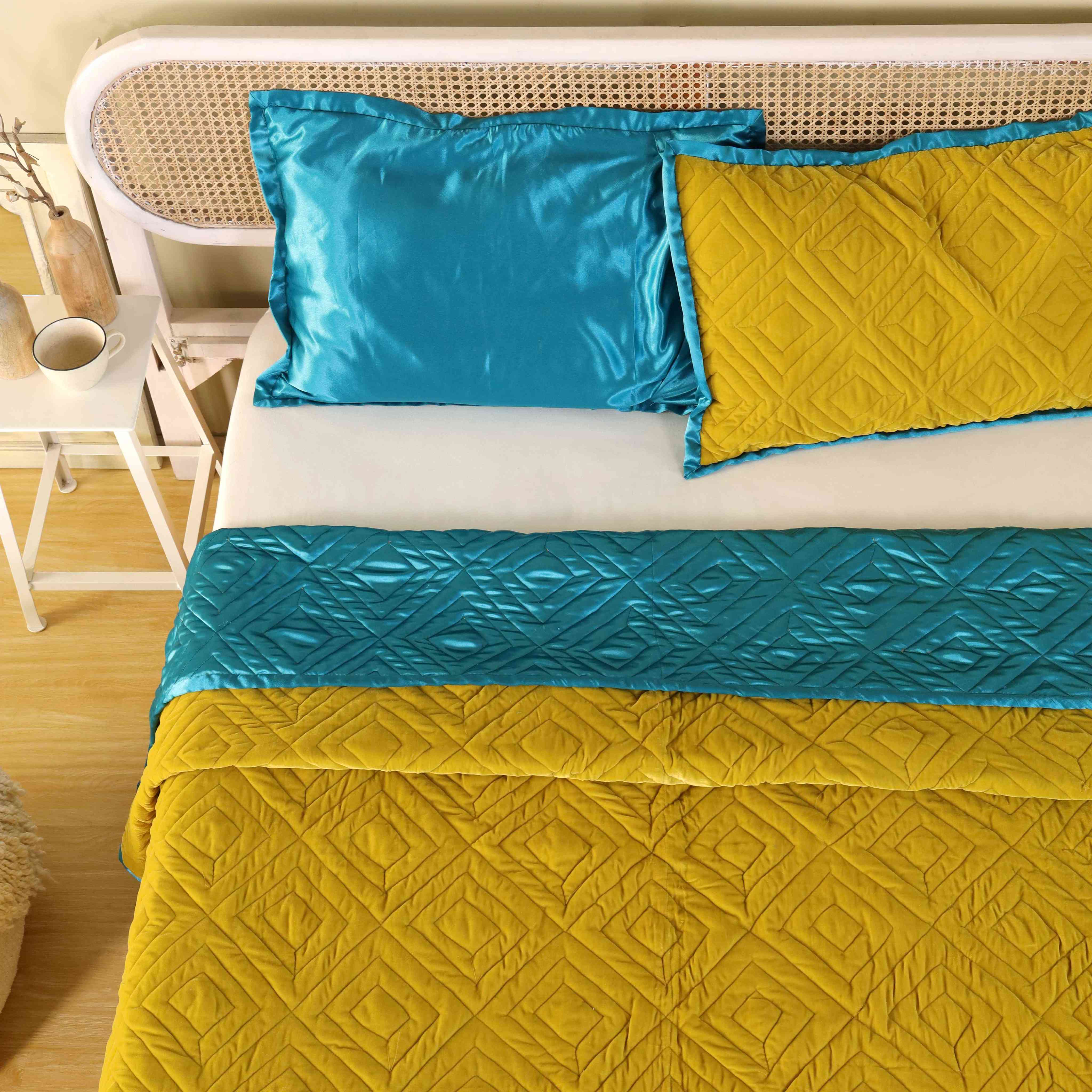 One teal satin pillow sham and one quilted mustard yellow sham on a bed.