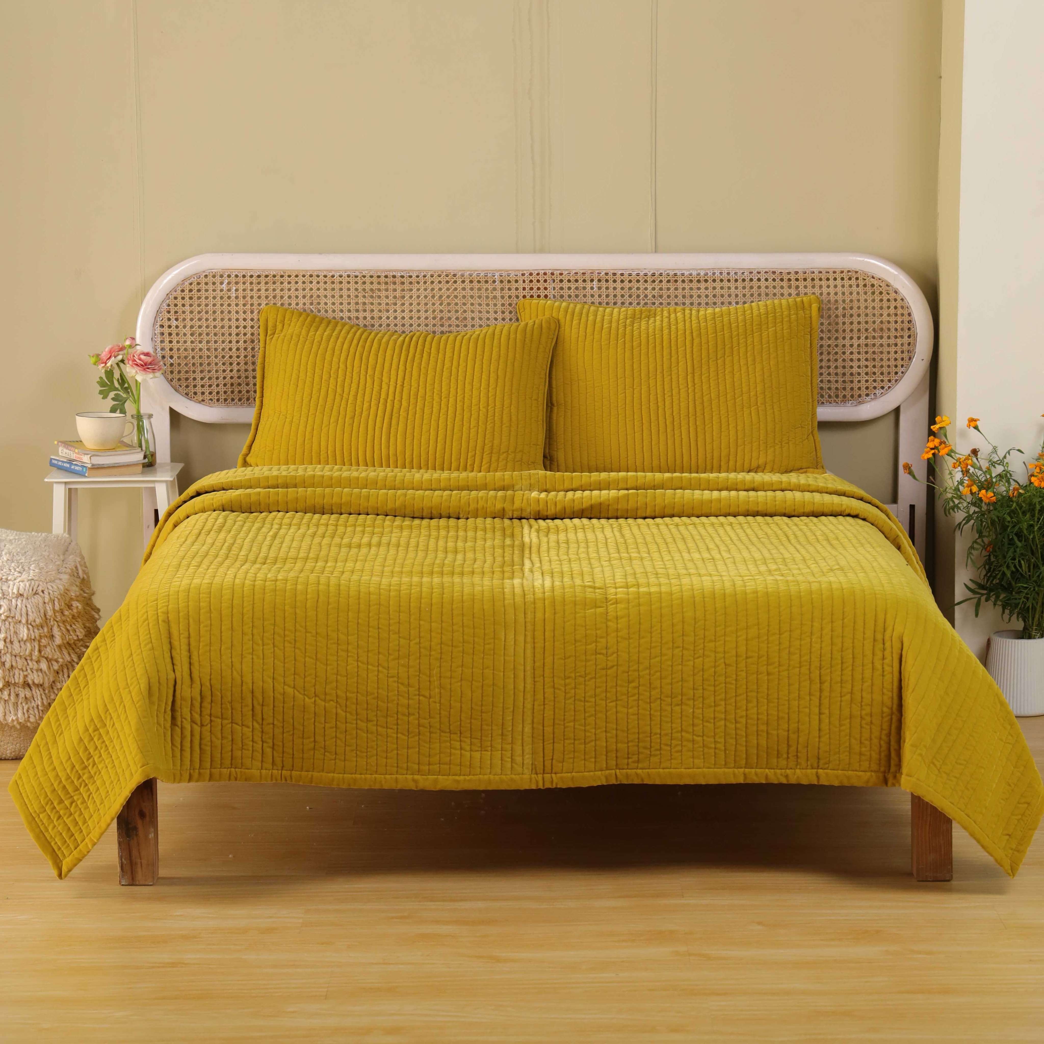 Mustard yellow velvet duvet cover set with vertical quilting on a bed with a white cane headboard.