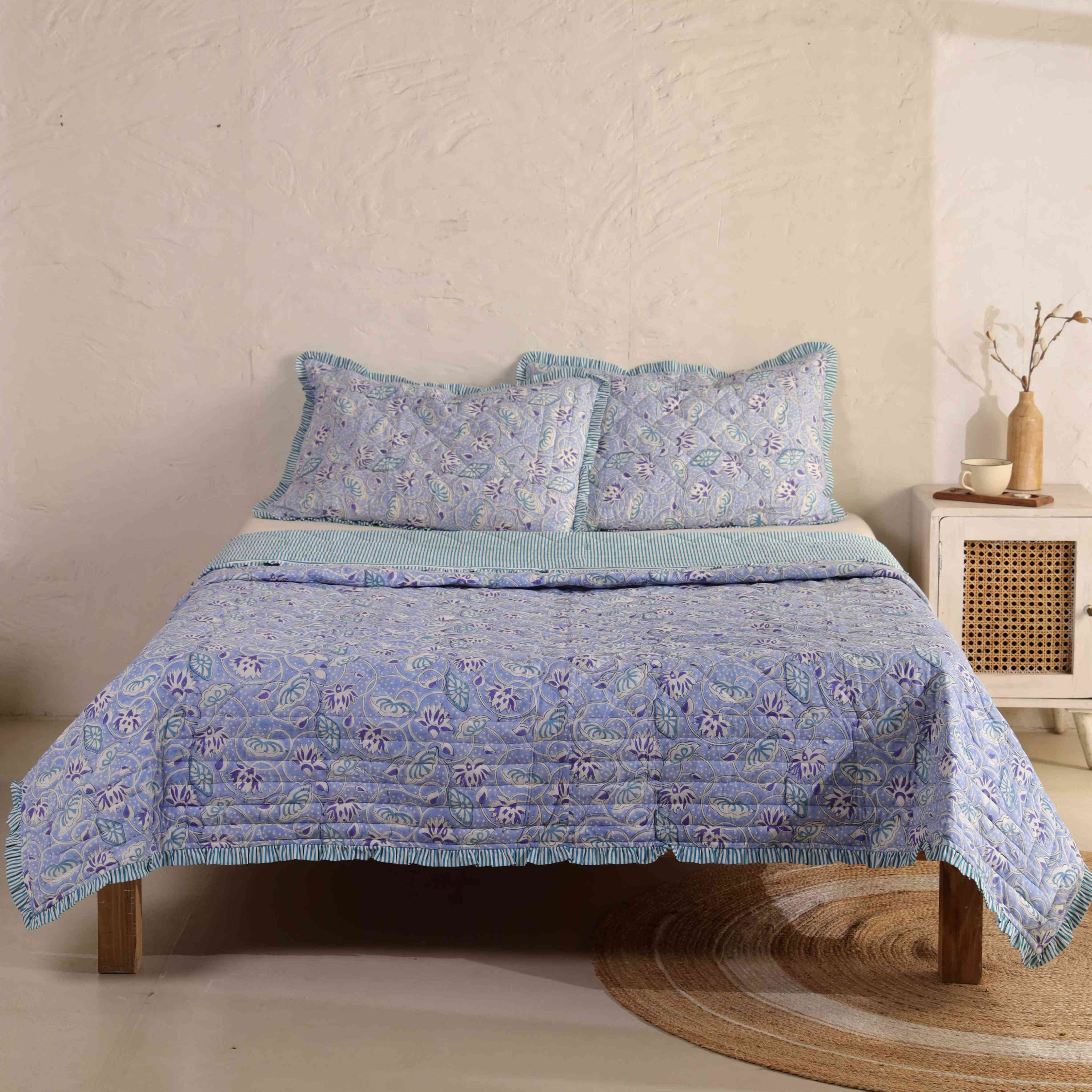 3-piece periwinkle blue floral cotton quilt set with ruffled edges on a bed.