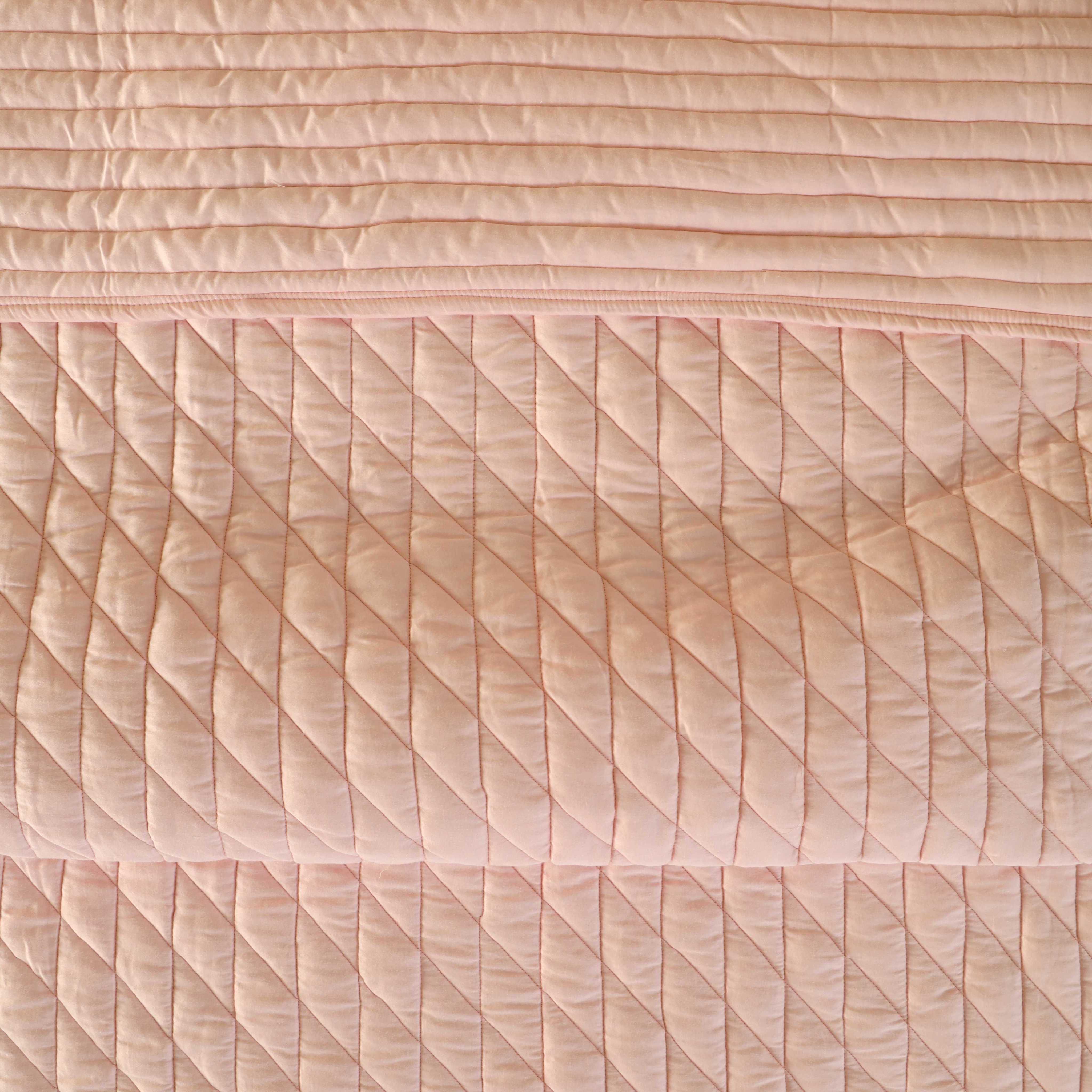 Close-up of the intricate floral and linear quilting on the pink satin fabric.