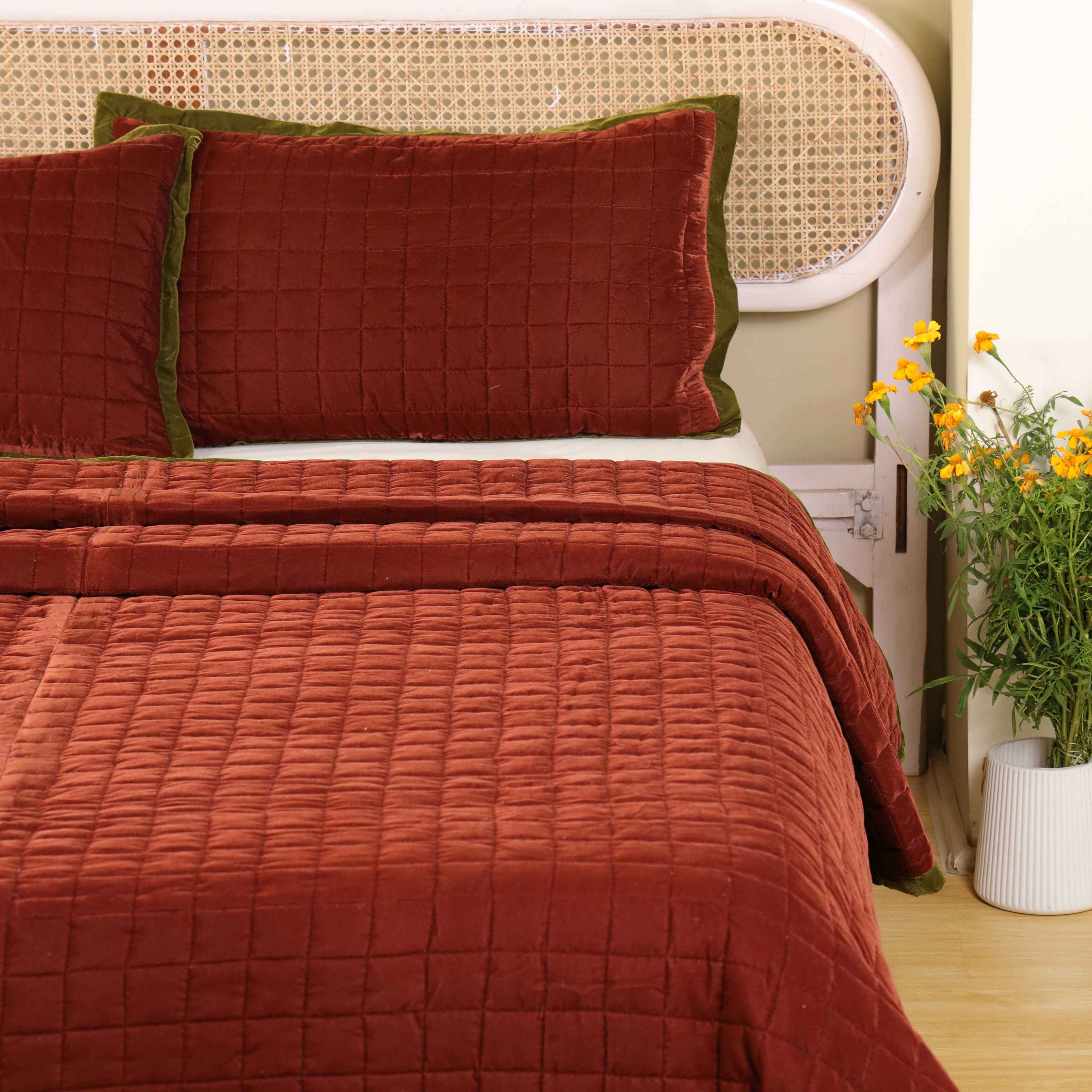Luxury quilted maroon bedding set styled in a bright minimalist bedroom with neutral walls.